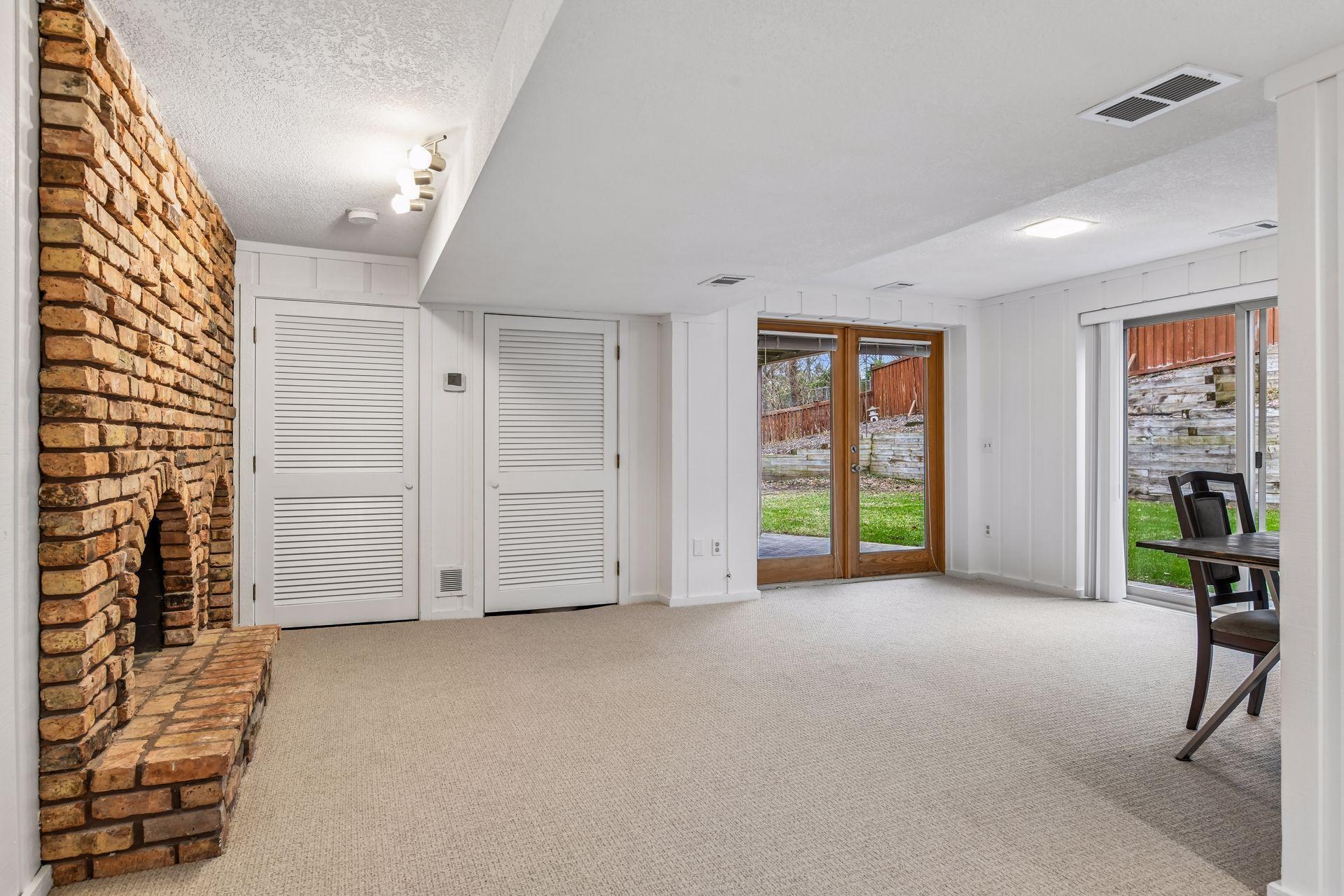 18x14 Lower-Level Flex Room with a wood-burning fireplace, new carpeting, and fresh paint. West-facing windows and walk-out doors