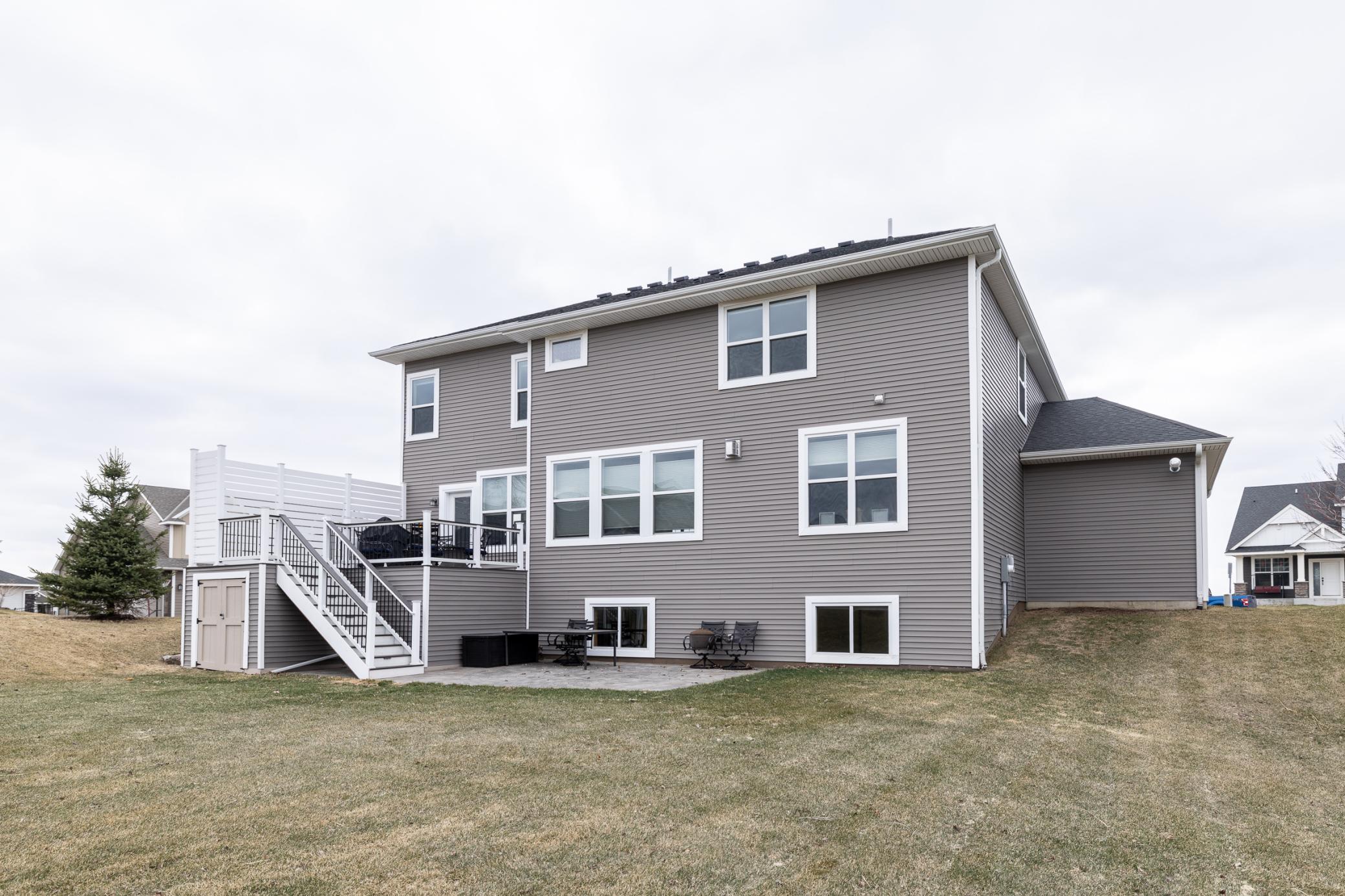 Rear exterior showcasing a spacious deck with built-in under-deck storage, walkout lower level, paver patio, and expansive backyard