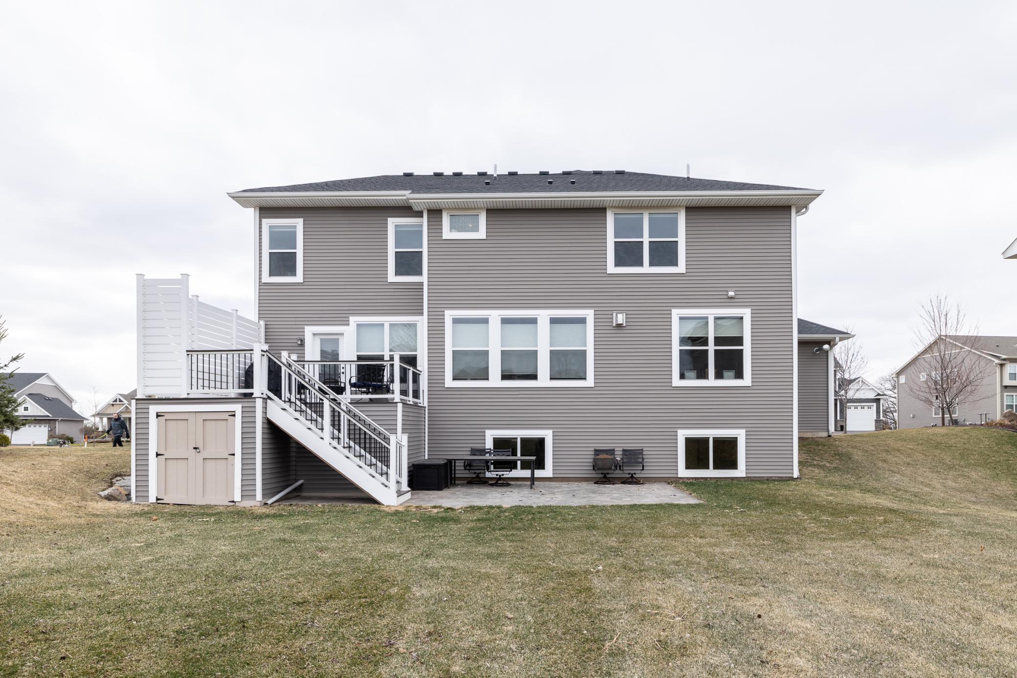 Rear exterior showcasing a spacious deck with built in storage below, walkout lower level, paver patio, and expansive backyard—ideal for outdoor living
