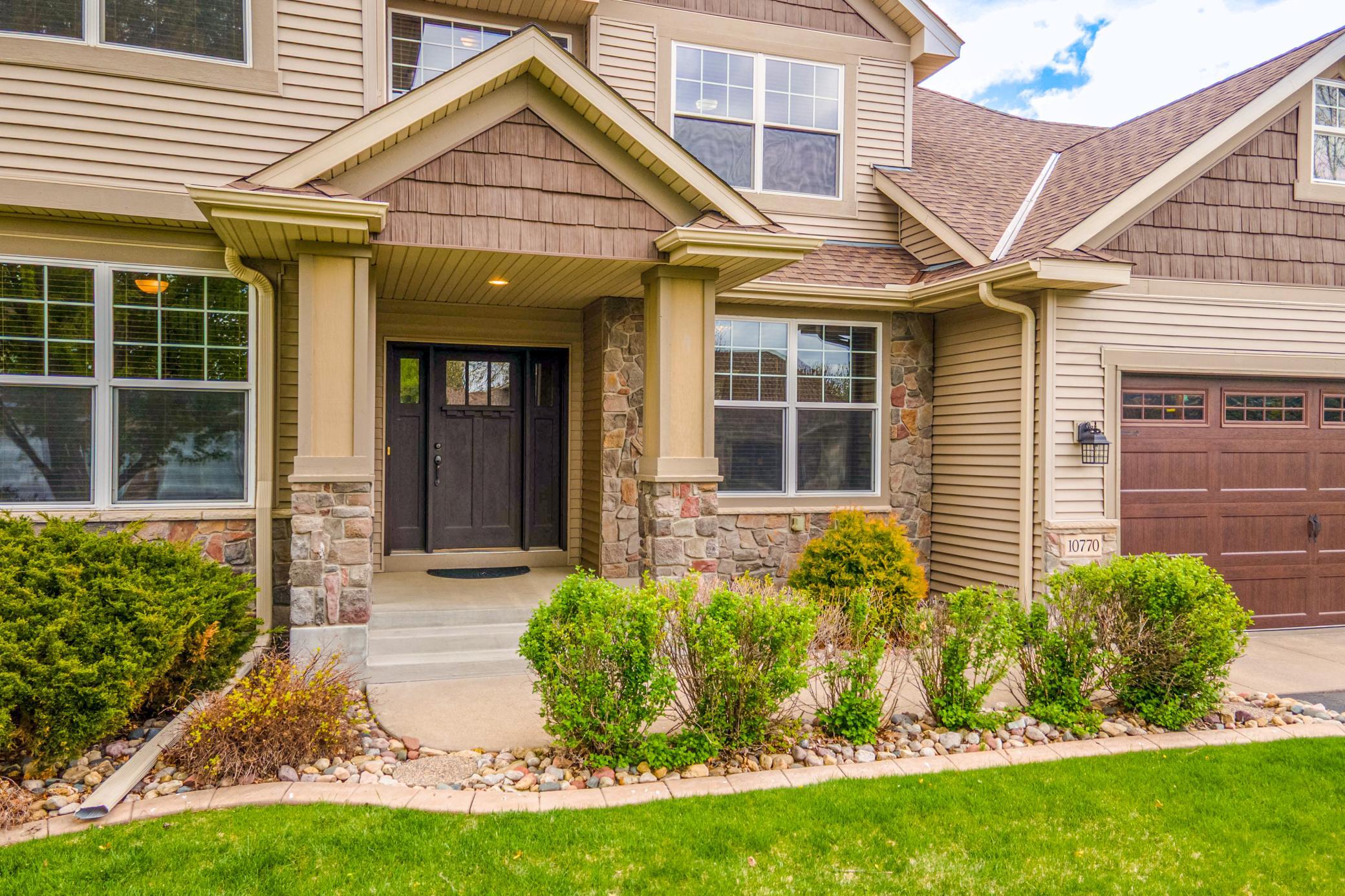Welcoming covered front entry with charming stonework, manicured landscaping, and elegant architectural details.