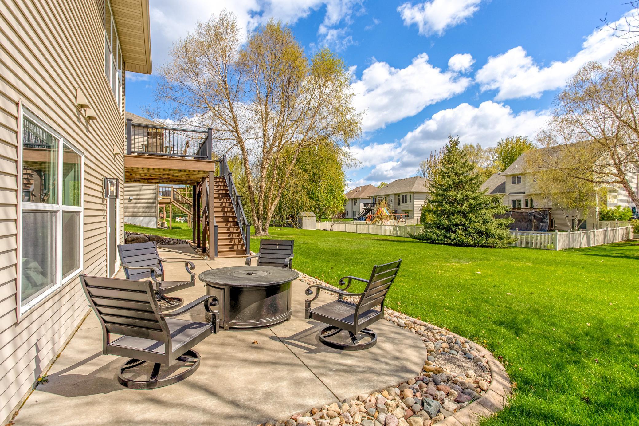 Lower-level patio with cozy fire pit seating area overlooking the expansive, tree-lined backyard.