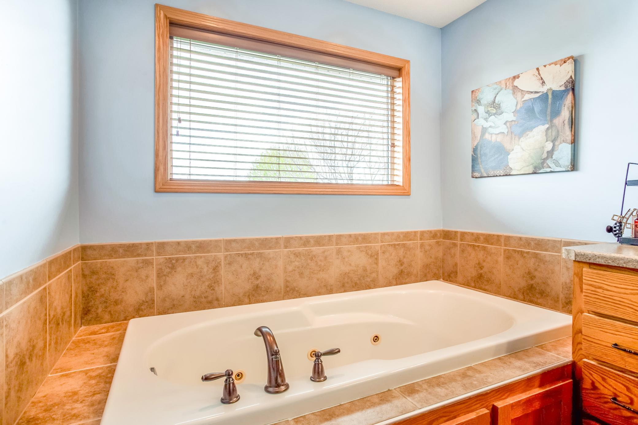 Relaxing jetted soaking tub surrounded by tile accents and large windows for a bright, spa-like experience.