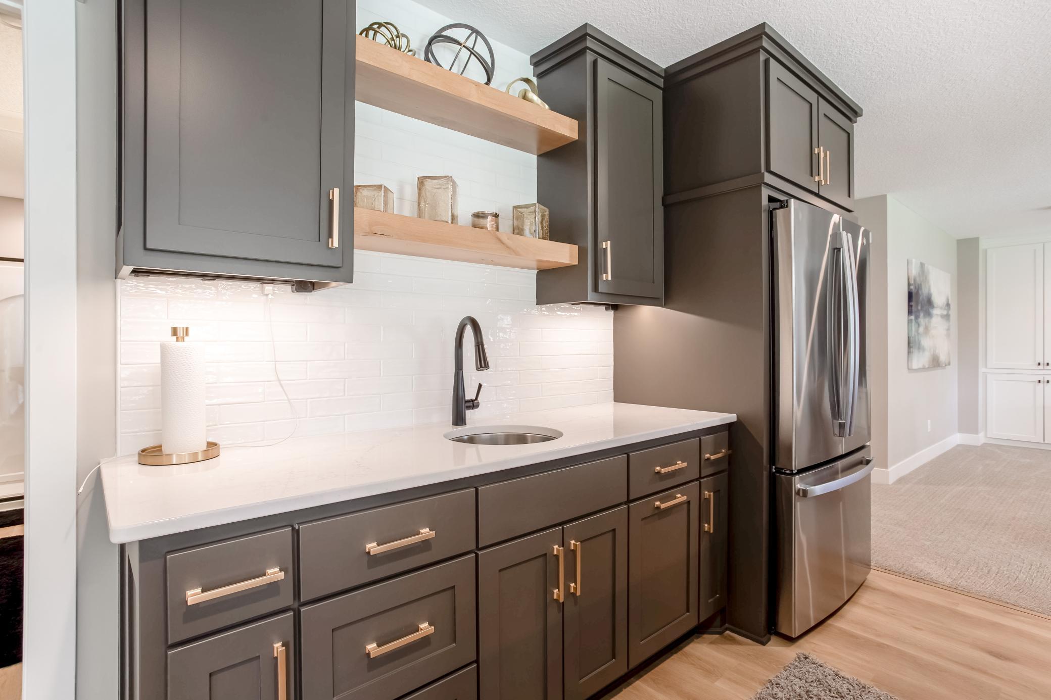Well-appointed lower-level wet bar with custom cabinetry, stainless steel refrigerator, and elegant designer details throughout.