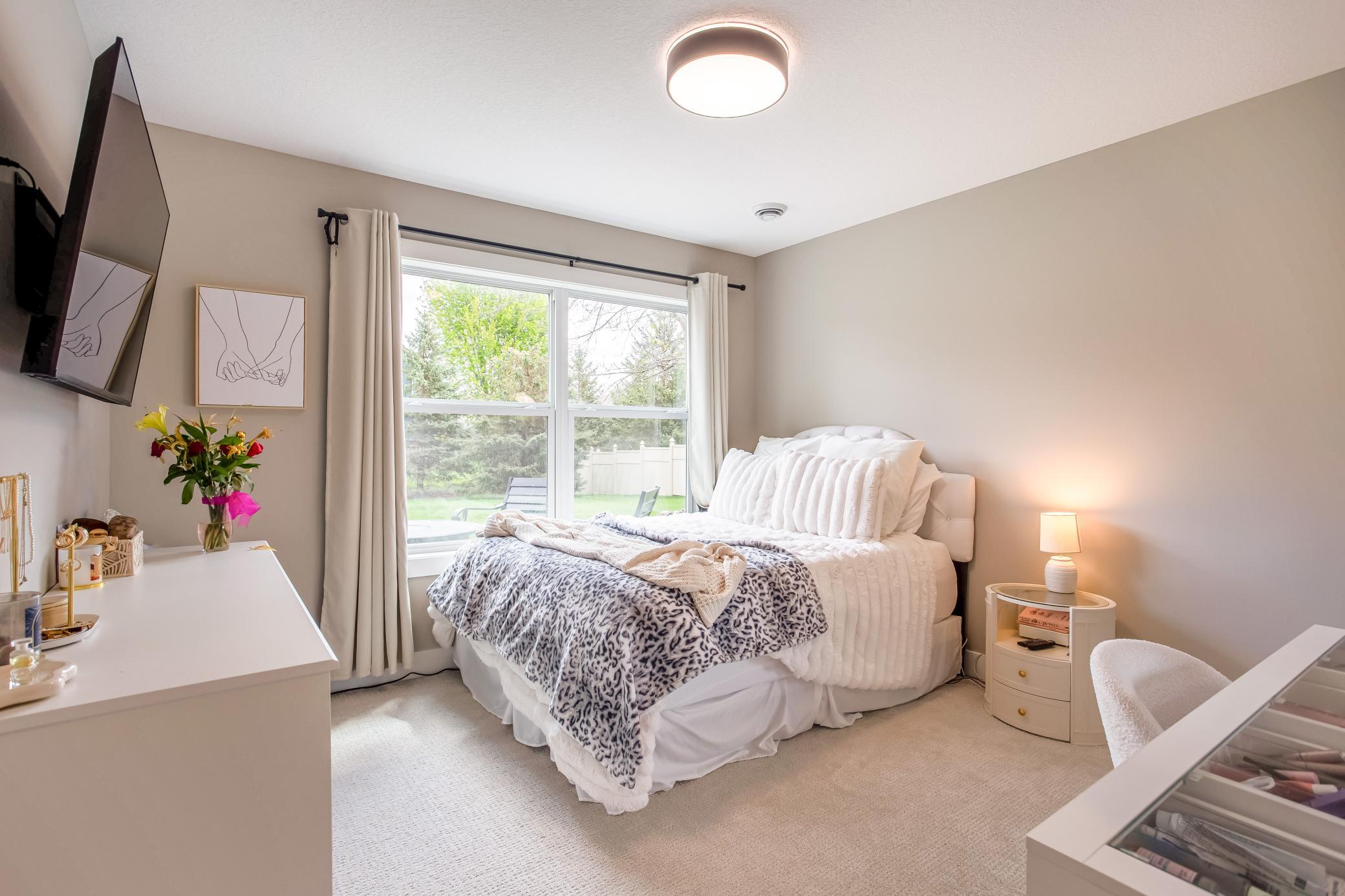 Comfortable lower-level bedroom with large windows, soft neutral finishes, and peaceful backyard views.