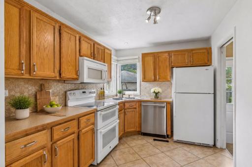 A functional kitchen featuring warm cabinetry, durable tile flooring, a neutral tile backsplash, and a window overlooking the backyard. **Virtually staged to show design options.**