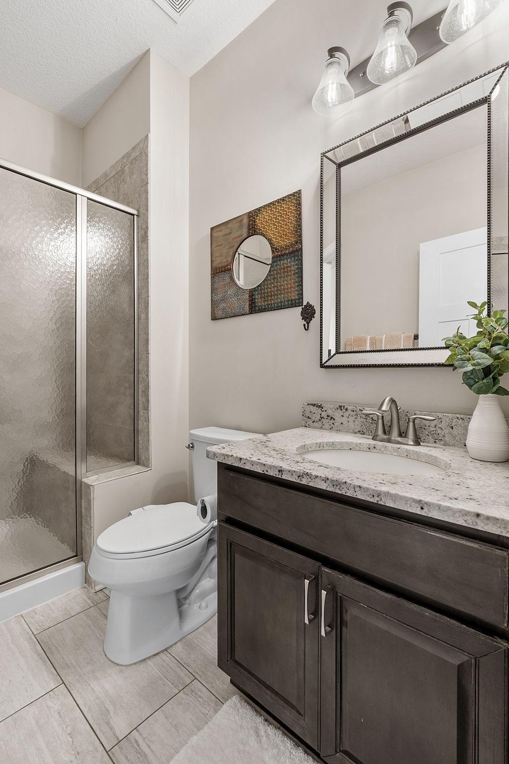 A second look at the spacious upper-level full bathroom showcases a deep-toned vanity with a premium granite top and modern fixture lighting.