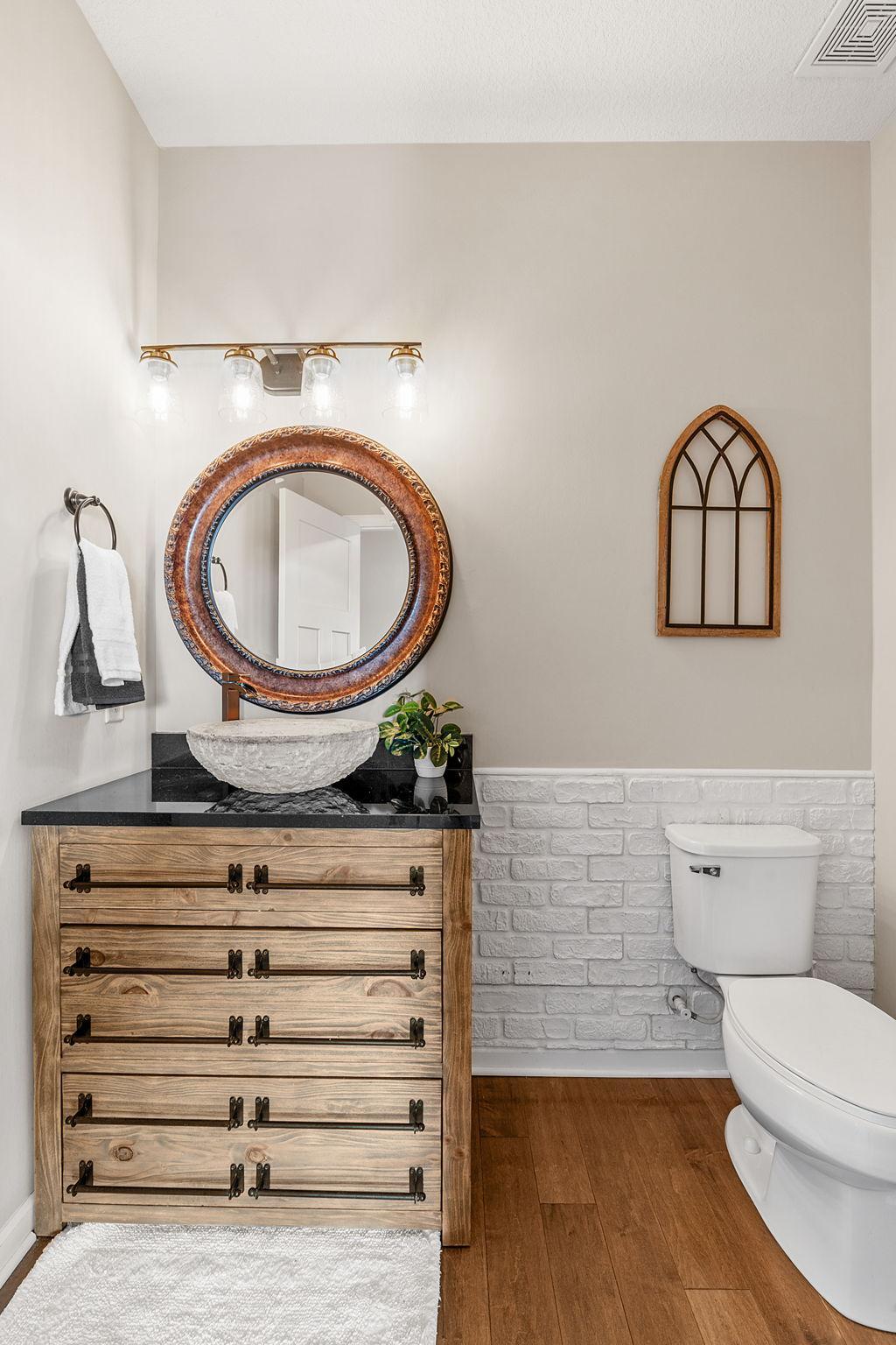 Another look at the guest bath showcases the beautiful textures, round bronze-accented mirror, and unique warm-toned cabinetry.