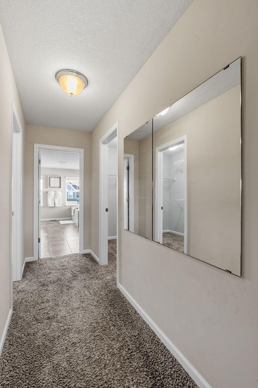 A private dressing hallway features large wall mirrors and direct access to separate walk-in closets before leading into the ensuite bath.