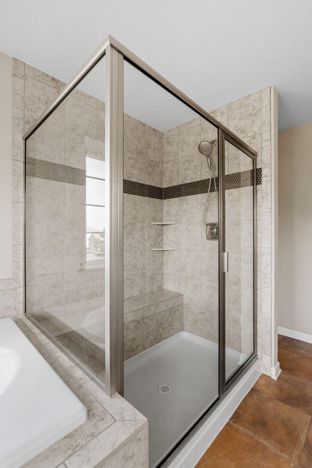 A closer look at the primary ensuite walk-in shower highlights the accent tile trim, integrated corner shelving, and convenient built-in bench seating.