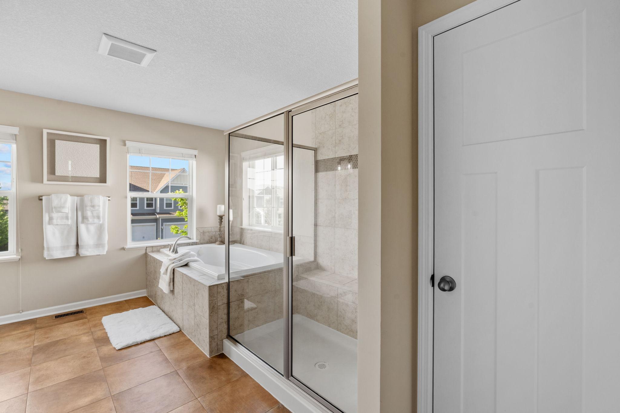 The separate glass shower enclosure features custom neutral tiling, a built-in bench seat, and clear sightlines across the expansive bathroom floor plan.