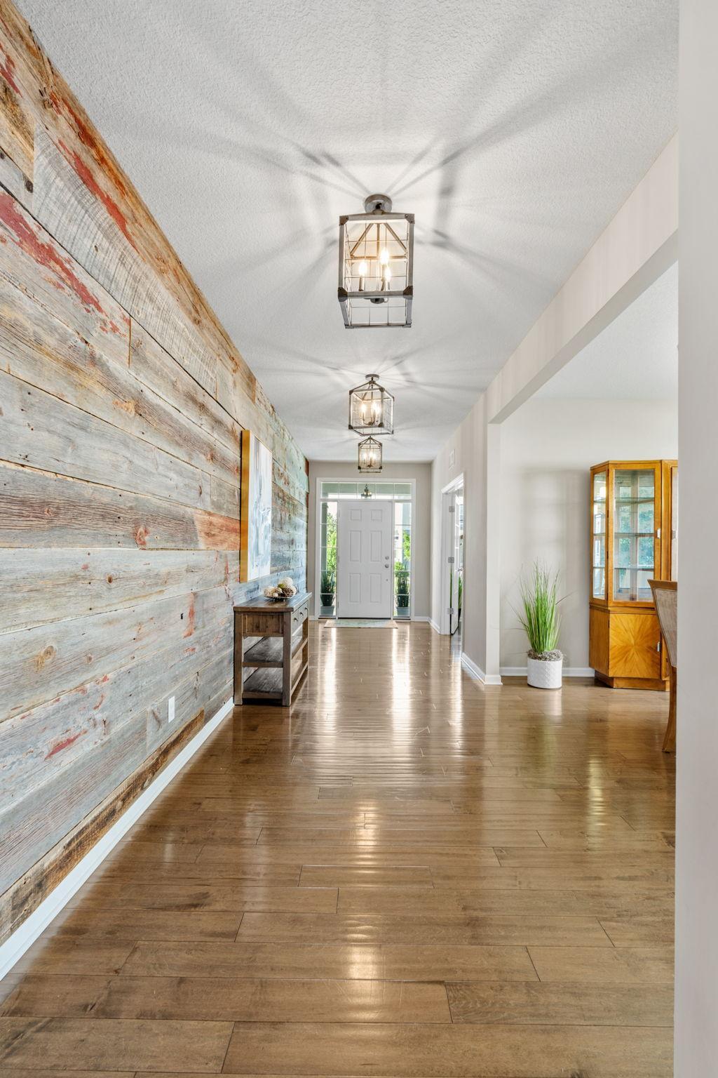 Step inside to a grand foyer featuring a gorgeous reclaimed-wood accent wall, gleaming hardwood floors, and modern geometric light fixtures.