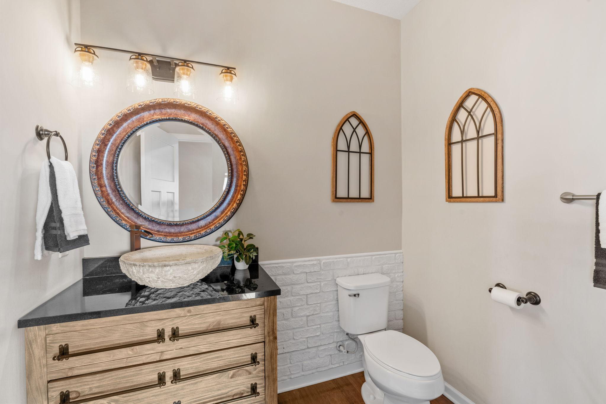 The main-floor half bath makes a statement with an organic stone vessel sink, a custom wood vanity, and stylish white-brick wainscoting.