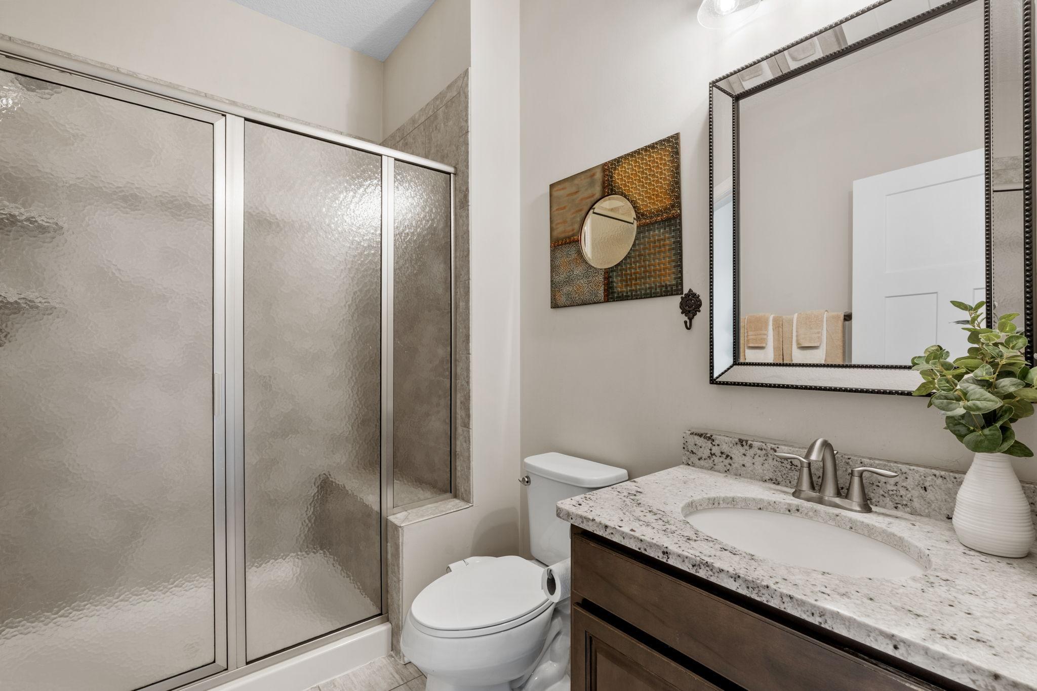 A beautifully updated upper-level bathroom, complete with a crisp granite-topped vanity, rich dark cabinetry, and a textured privacy-glass shower enclosure.