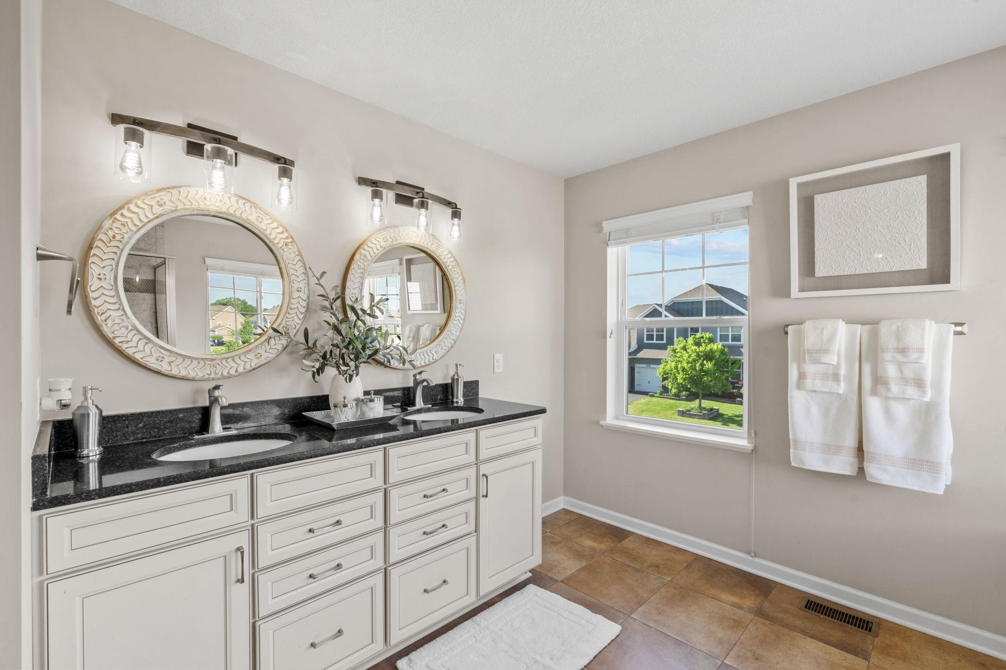 Pamper yourself in the primary bathroom, complete with a long double vanity, dark granite countertops, ornate mirrors, and stylish tile flooring.