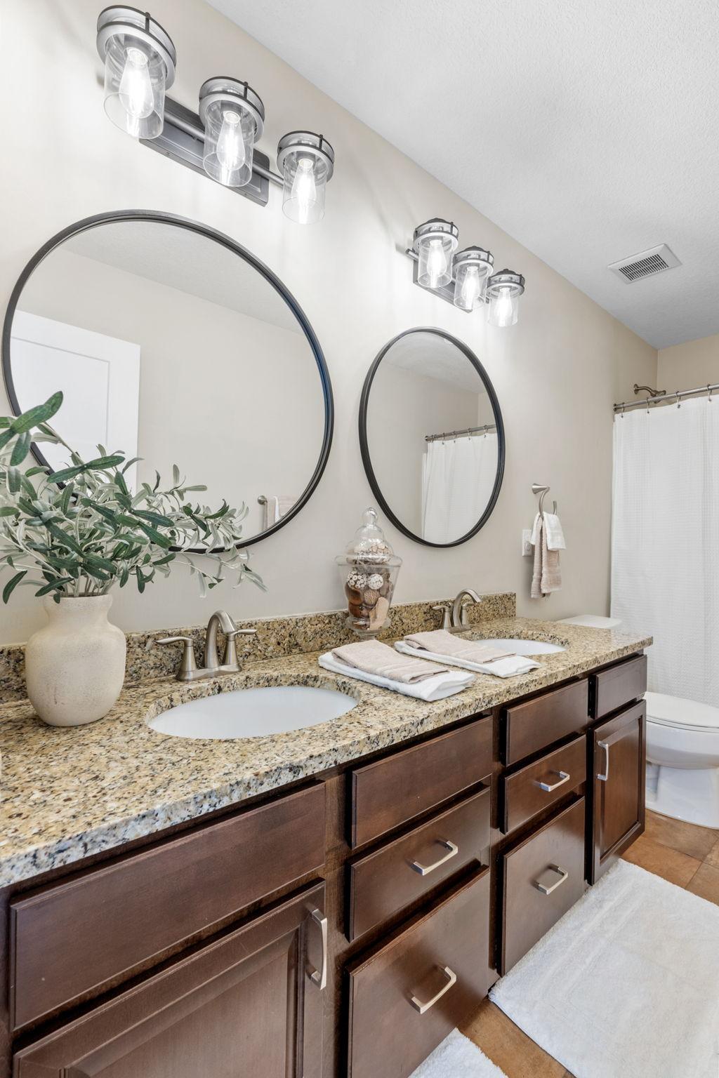 A closer angle of the upper-level full bath features extensive drawer storage, a sleek granite countertop, and clear glass vanity lighting.