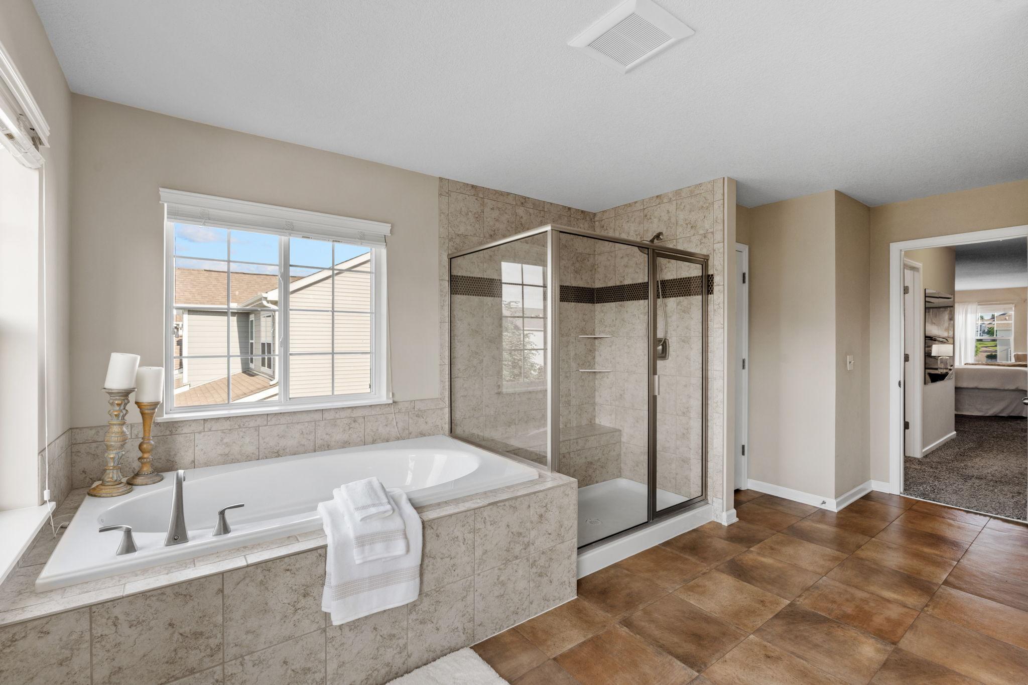 The ensuite boasts a deep tile-surround soaking tub positioned under a bright window, alongside a separate glass-enclosed walk-in shower.