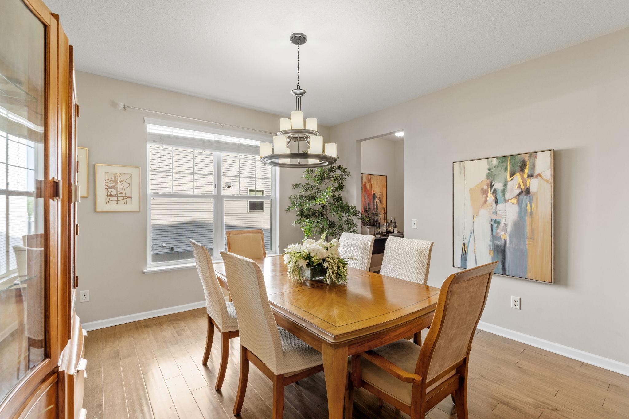 The sophisticated formal dining room features rich hardwood flooring, a statement chandelier, and a bright window filling the room with natural light.