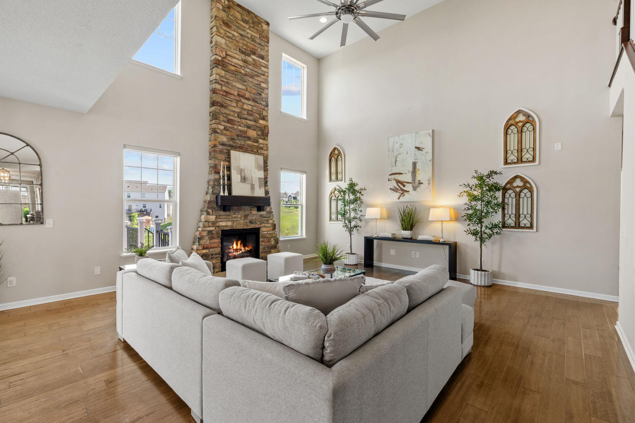 The living room's magnificent focal point features a massive floor-to-ceiling stone fireplace surrounded by large windows.