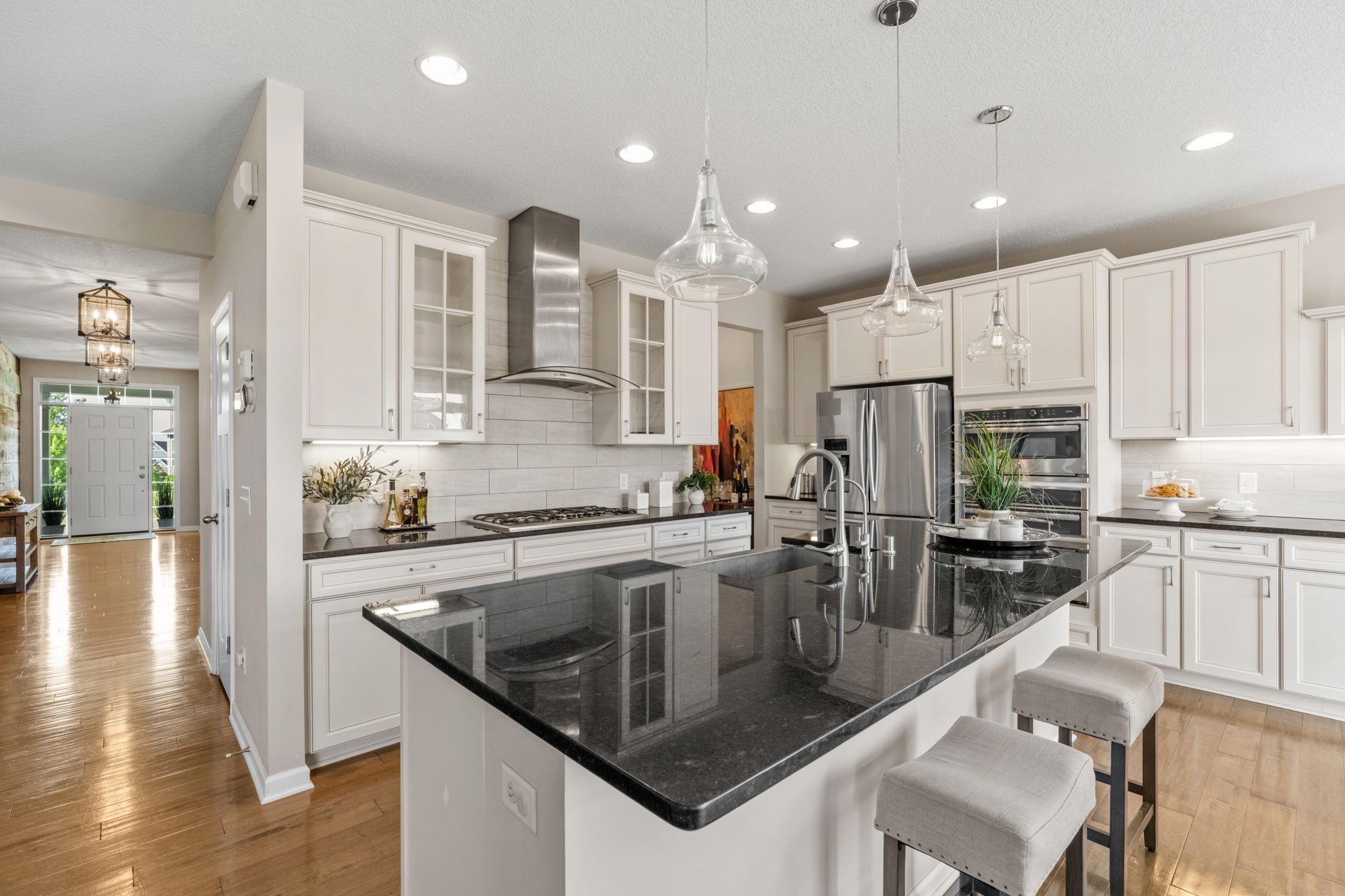 View from the casual dining area highlights the kitchen's vast footprint, breakfast bar seating, and stylish pendant lighting.