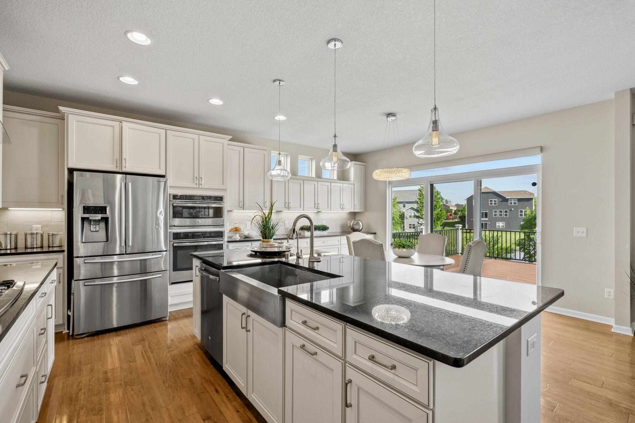 The heart of the home features premium stainless steel appliances, double wall ovens, crisp white cabinetry, and an oversized central island with an apron-front sink.