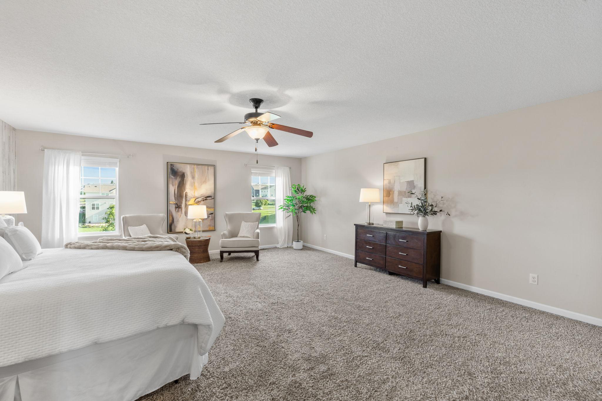 Large windows flood the bedroom with natural light, offering a perfect corner layout for a cozy private reading or sitting area.