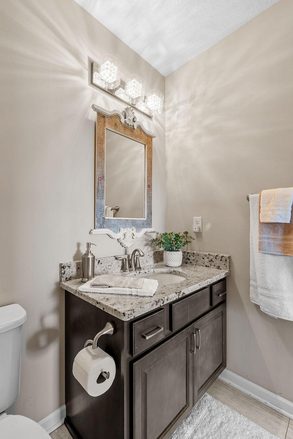 Another view highlights the beautiful neutral granite patterns, brushed nickel fixtures, and premium vanity lighting.