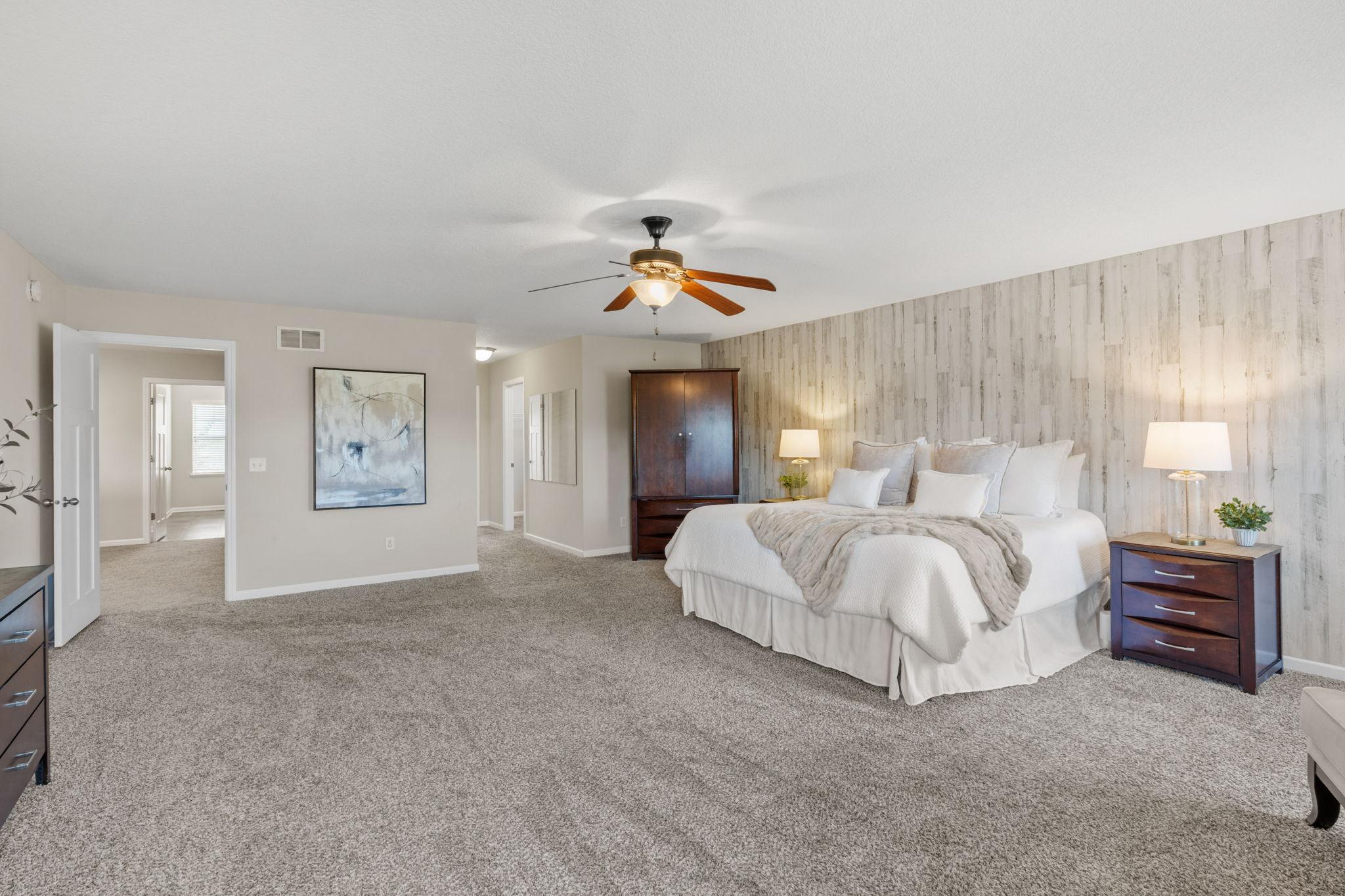 The massive primary bedroom serves as a true retreat, highlighting a rustic whitewashed wood accent wall, plush carpeting, and dual hallway entryways.