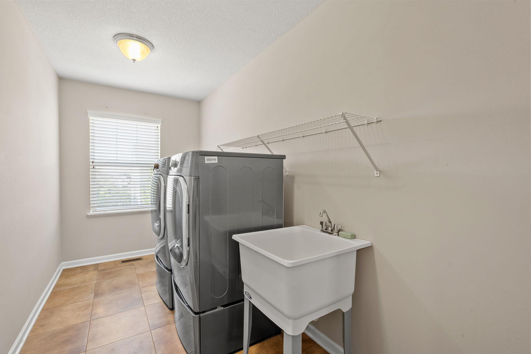 The convenient upper-level laundry room comes fully equipped with a deep utility sink, overhead wire shelving, and durable tile flooring.