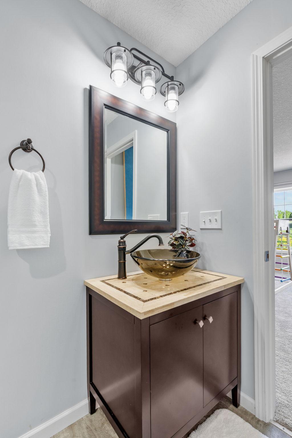 The lower-level bathroom showcases a beautiful, dark-stained vanity cabinet topped with an amber glass vessel bowl sink and an oil-rubbed bronze waterfall faucet.