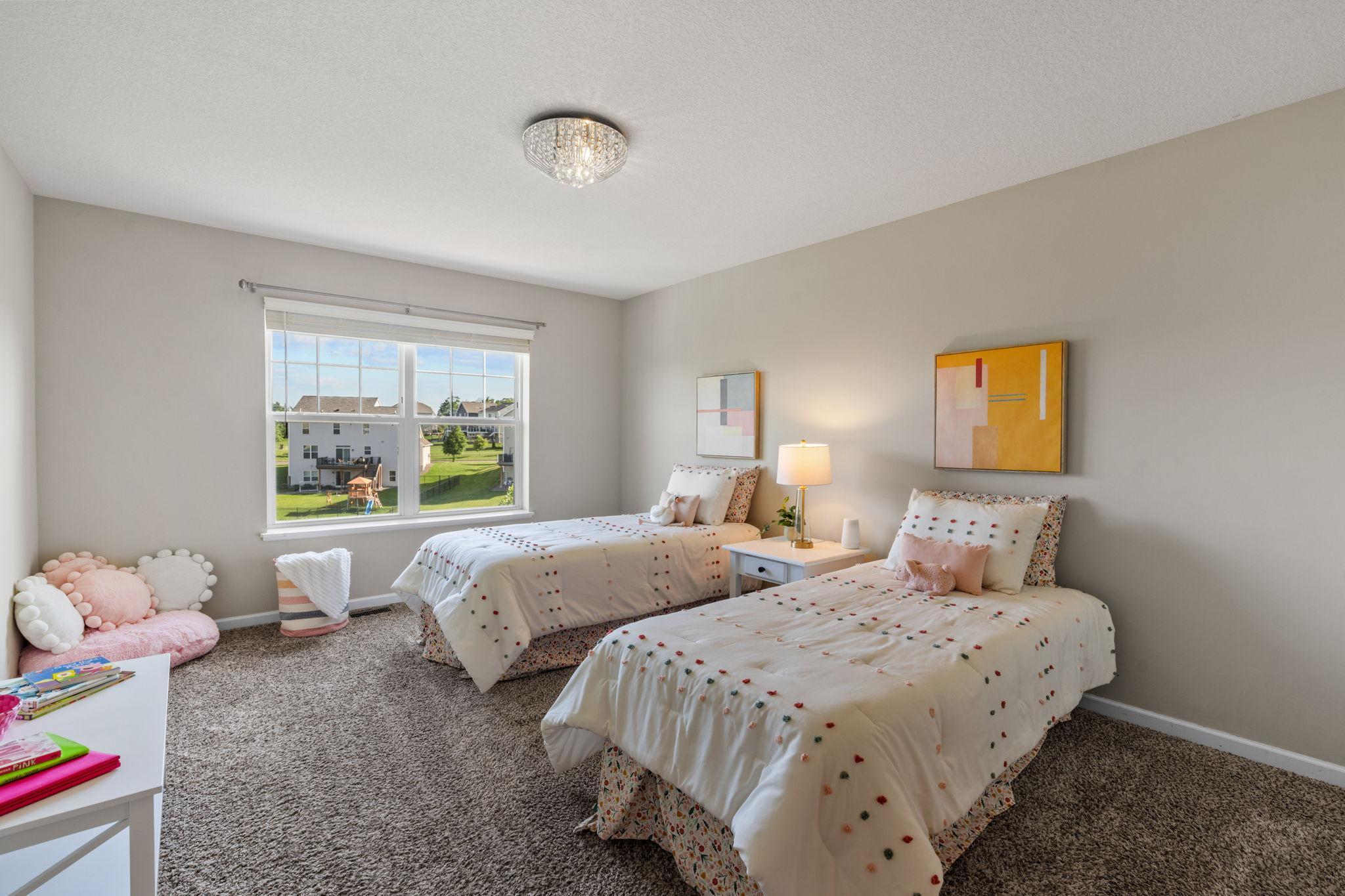 This bright and cheerful secondary bedroom offers ample square footage, a large window with green backyard views, and a crystal accent light fixture.