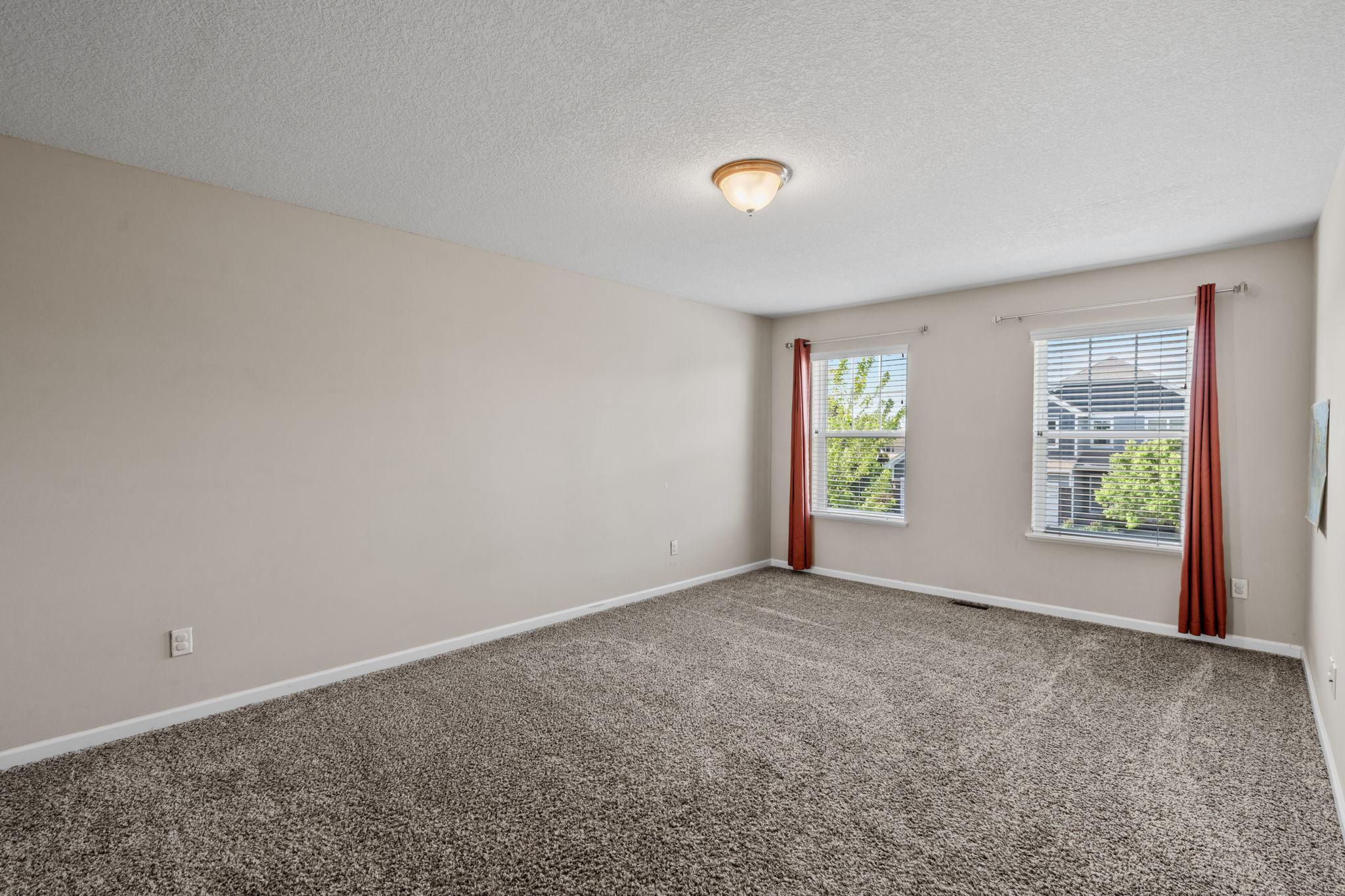 A second upper-level bedroom offers generous square footage, plush carpeting, and dual windows drawing in ample daylight.