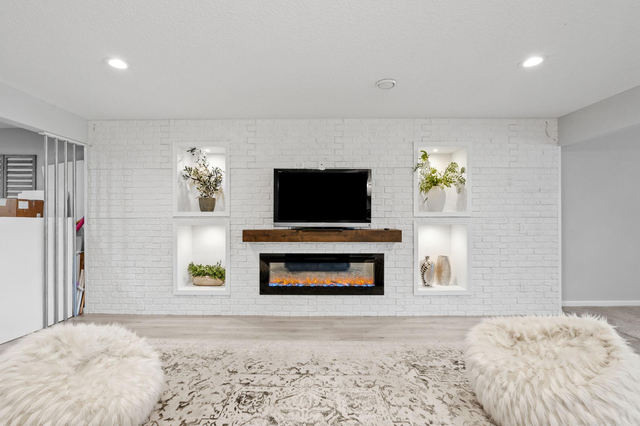 A striking white brick accent wall anchors the lower-level rec room, complete with a floating wood mantle and an integrated sleek electric fireplace.