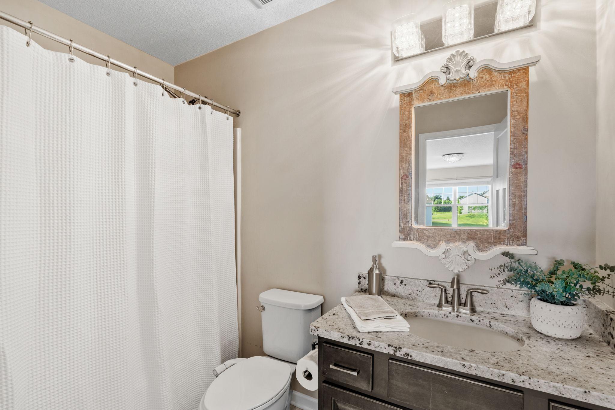 Serving the upper secondary bedrooms, this pristine bathroom includes a dark wood vanity, granite counters, and a unique ornate mirror frame.