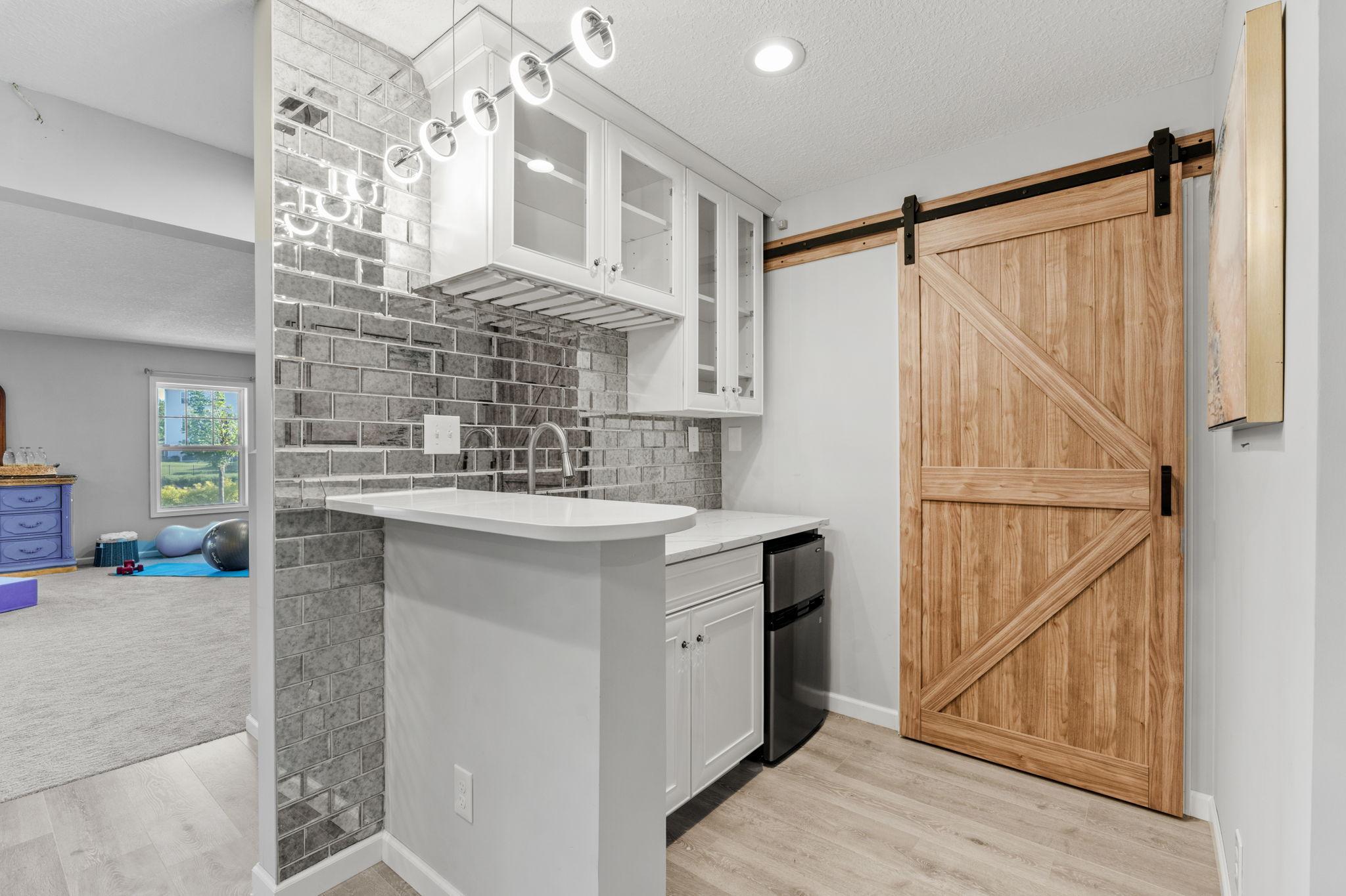 Entertain with ease using this stylish beverage station, featuring a striking antique mirrored-brick backsplash, crisp white cabinets, and a mini-fridge.