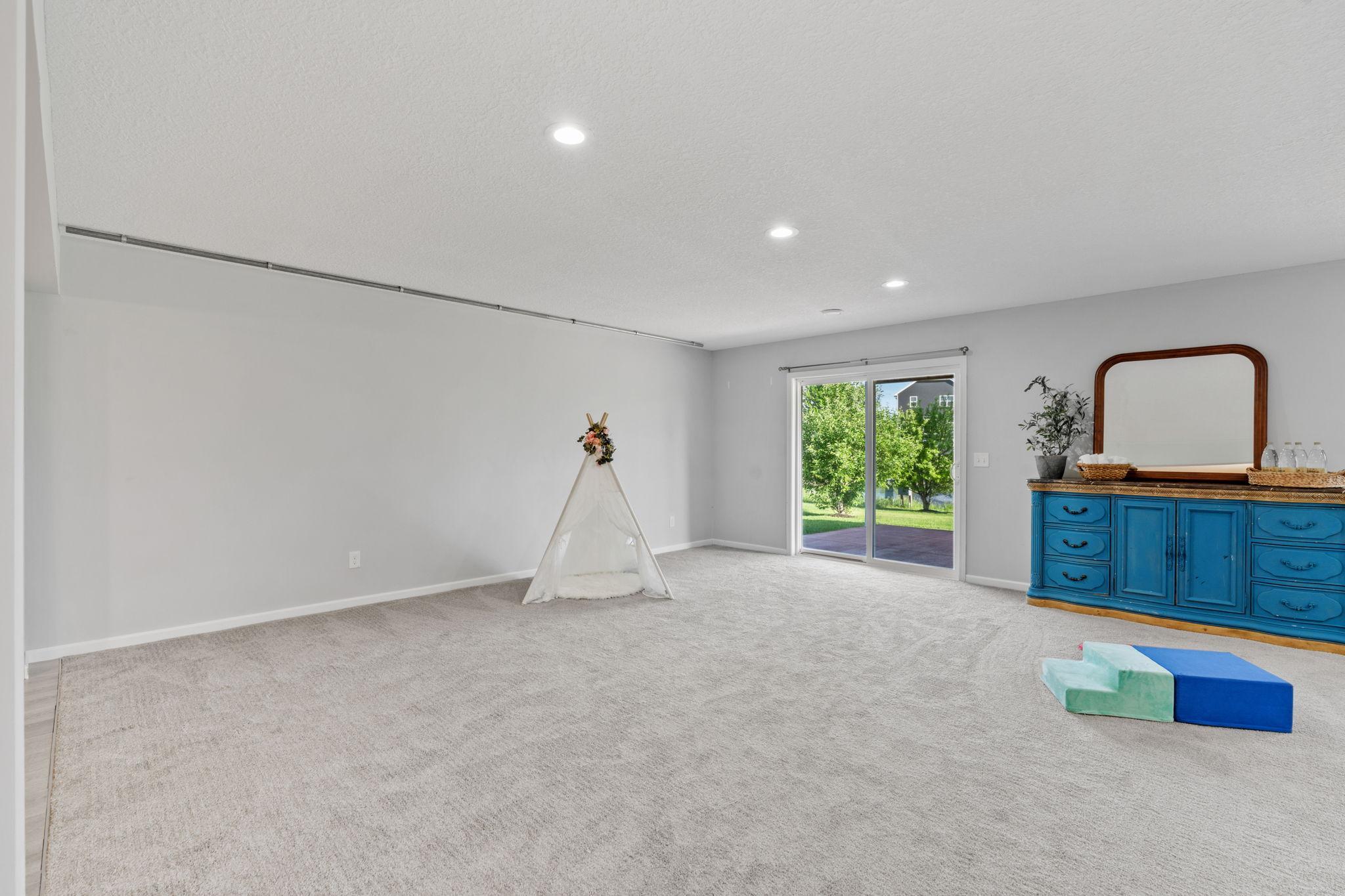 Plush neutral carpeting transitions to a massive play or fitness zone, flooded with natural light from large sliding glass doors that lead out to the backyard.