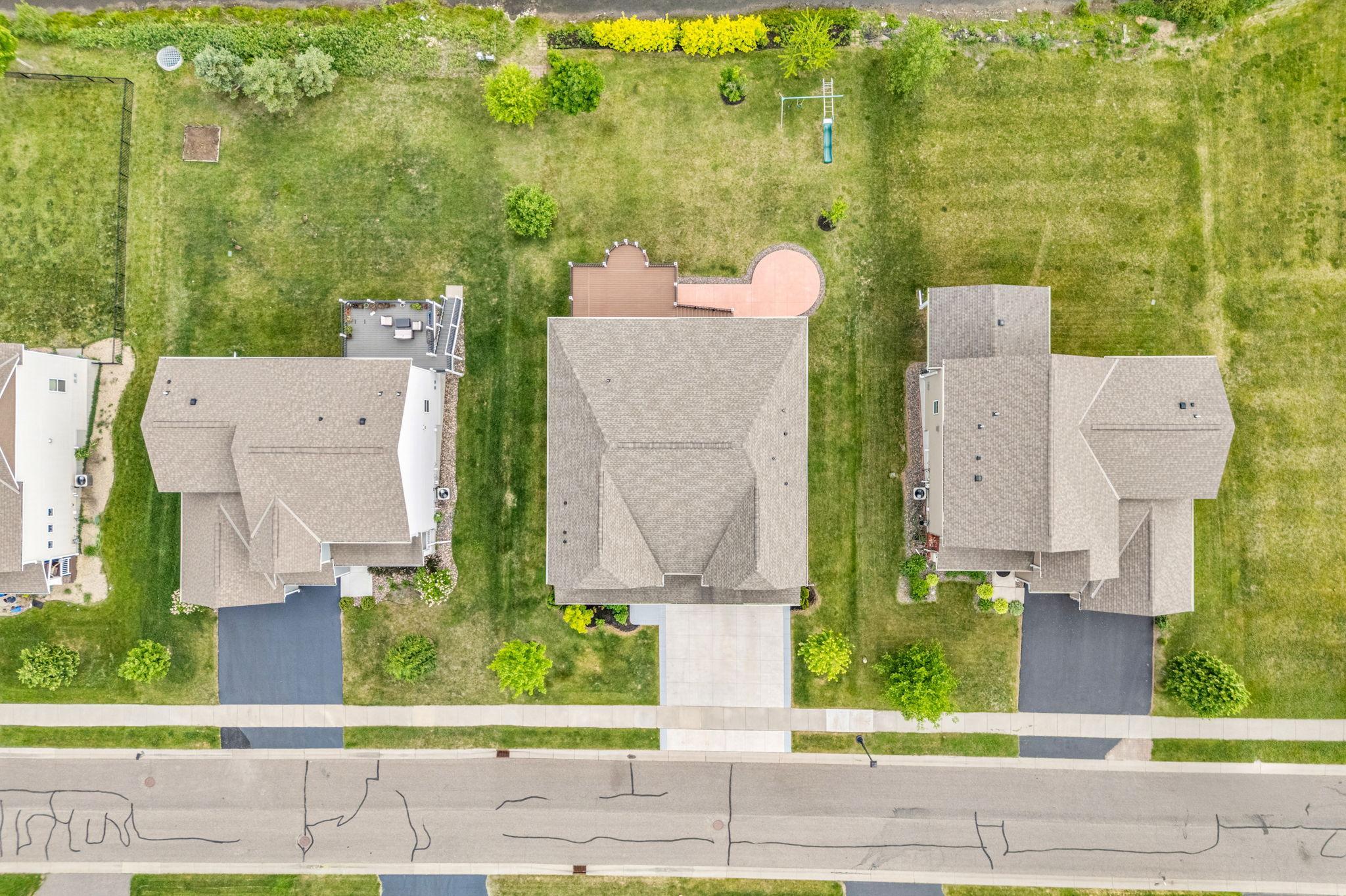 A straight-down aerial shot highlights the spacious roofline, property boundaries, custom patio shape, and deep backyard layout.