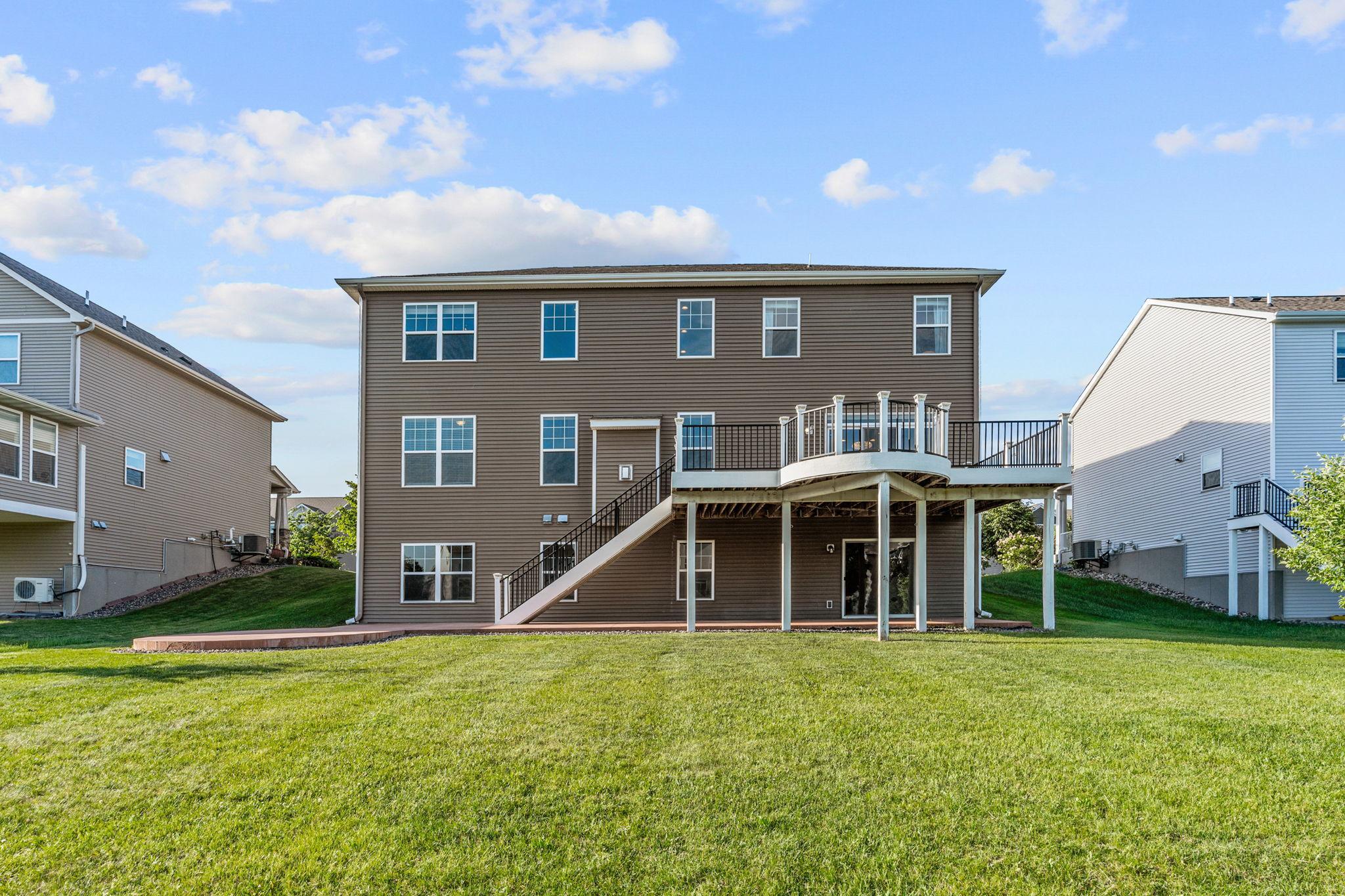 An impressive view from the lawn showcases the grand scale of the property, highlighting the unique curved bump-out deck design, built-in staircase, and endless space for recreation.