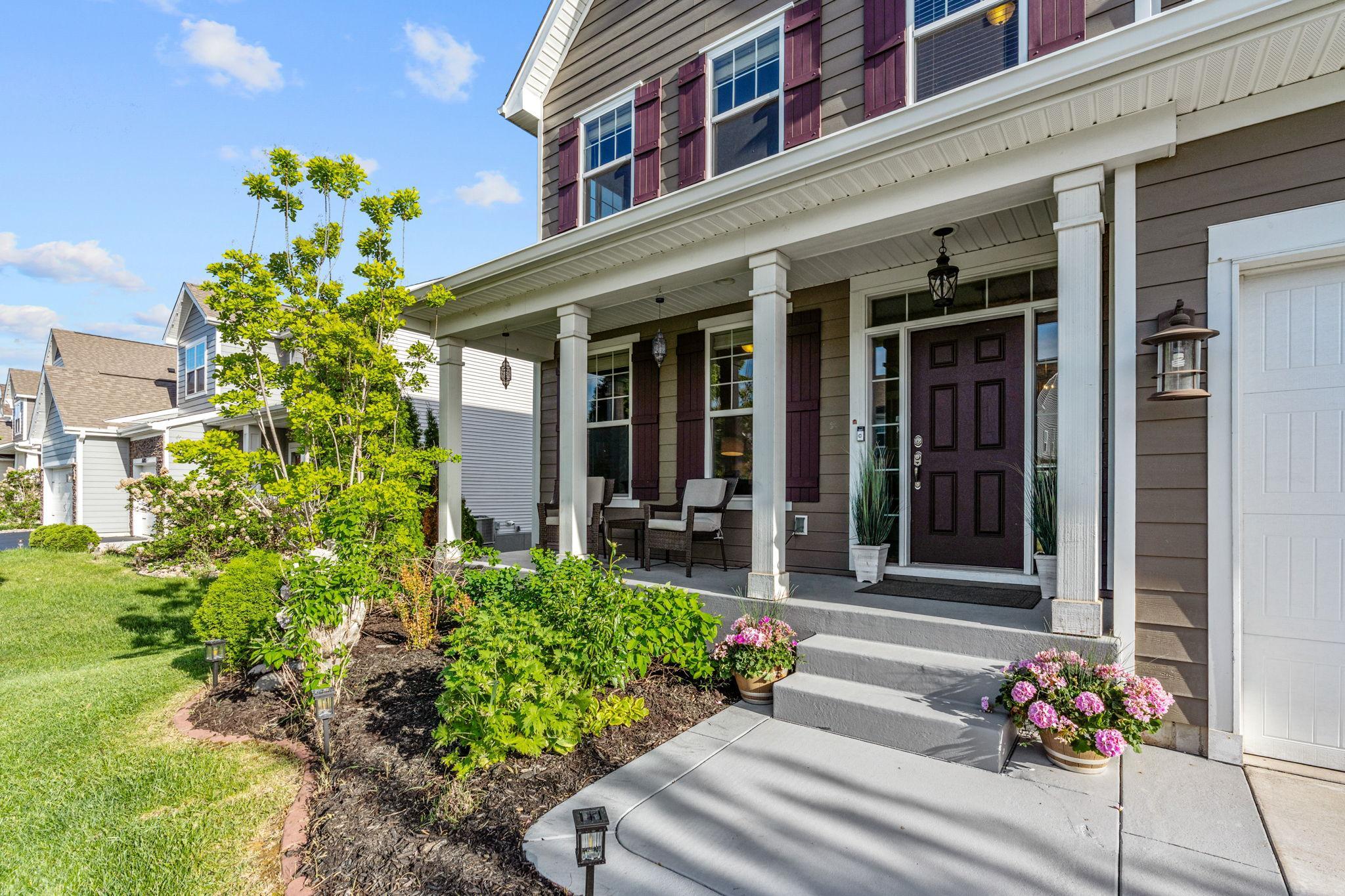 Step up to the inviting covered front entryway, complete with crisp white pillars, space for comfortable outdoor seating, and meticulously maintained flowerbeds.