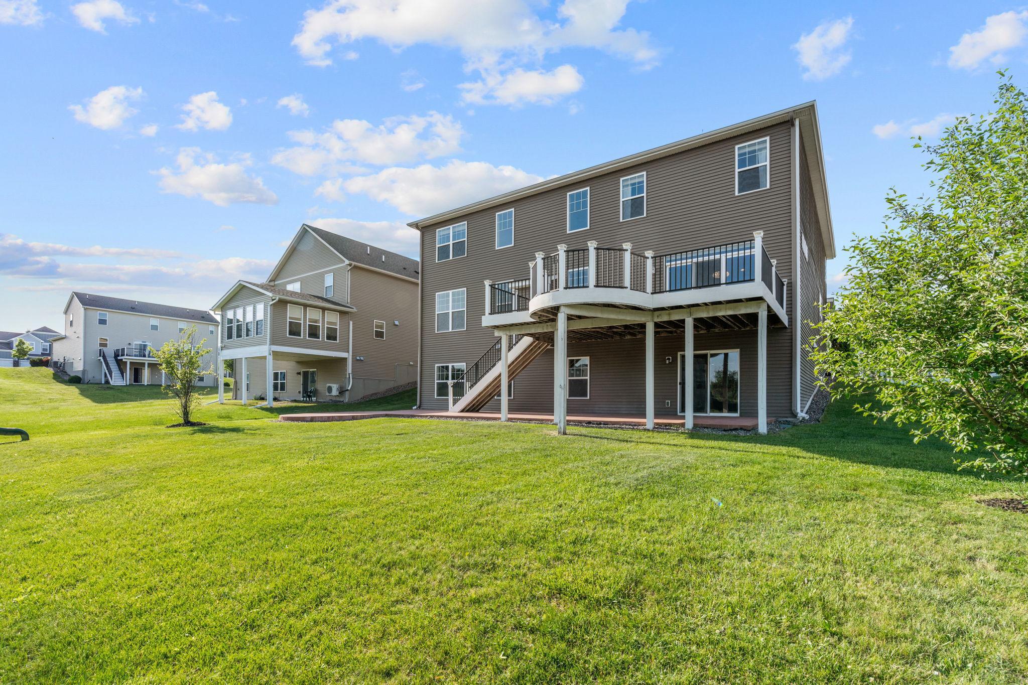 The rear of the home reveals a massive, sprawling green lawn, a sweeping walkout basement layout, and a magnificent elevated deck overlooking the yard