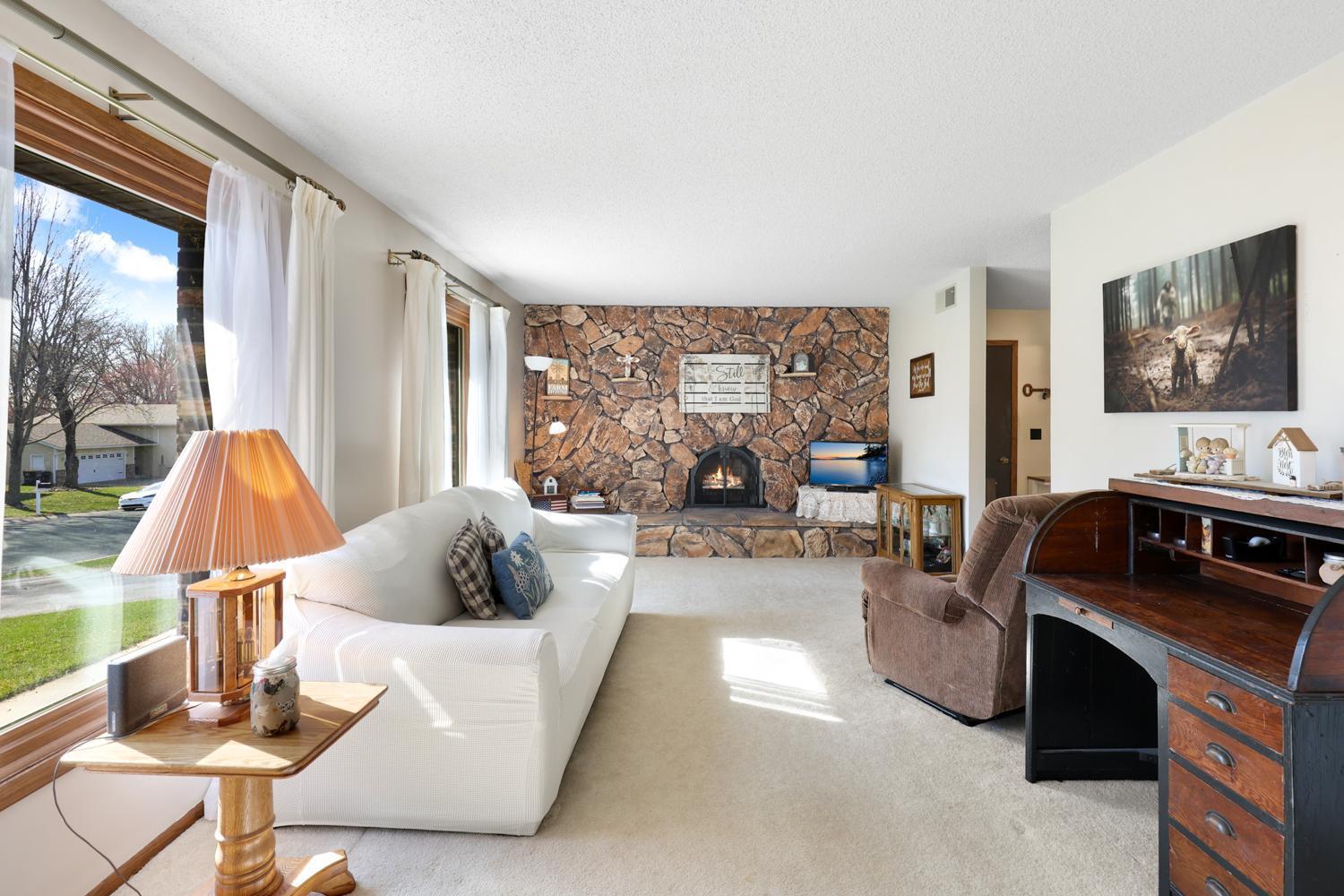 Light-filled living room with large windows and a stunning floor-to-ceiling stone fireplace that creates a warm, inviting focal point. A perfect space to unwind or gather with friends and family.