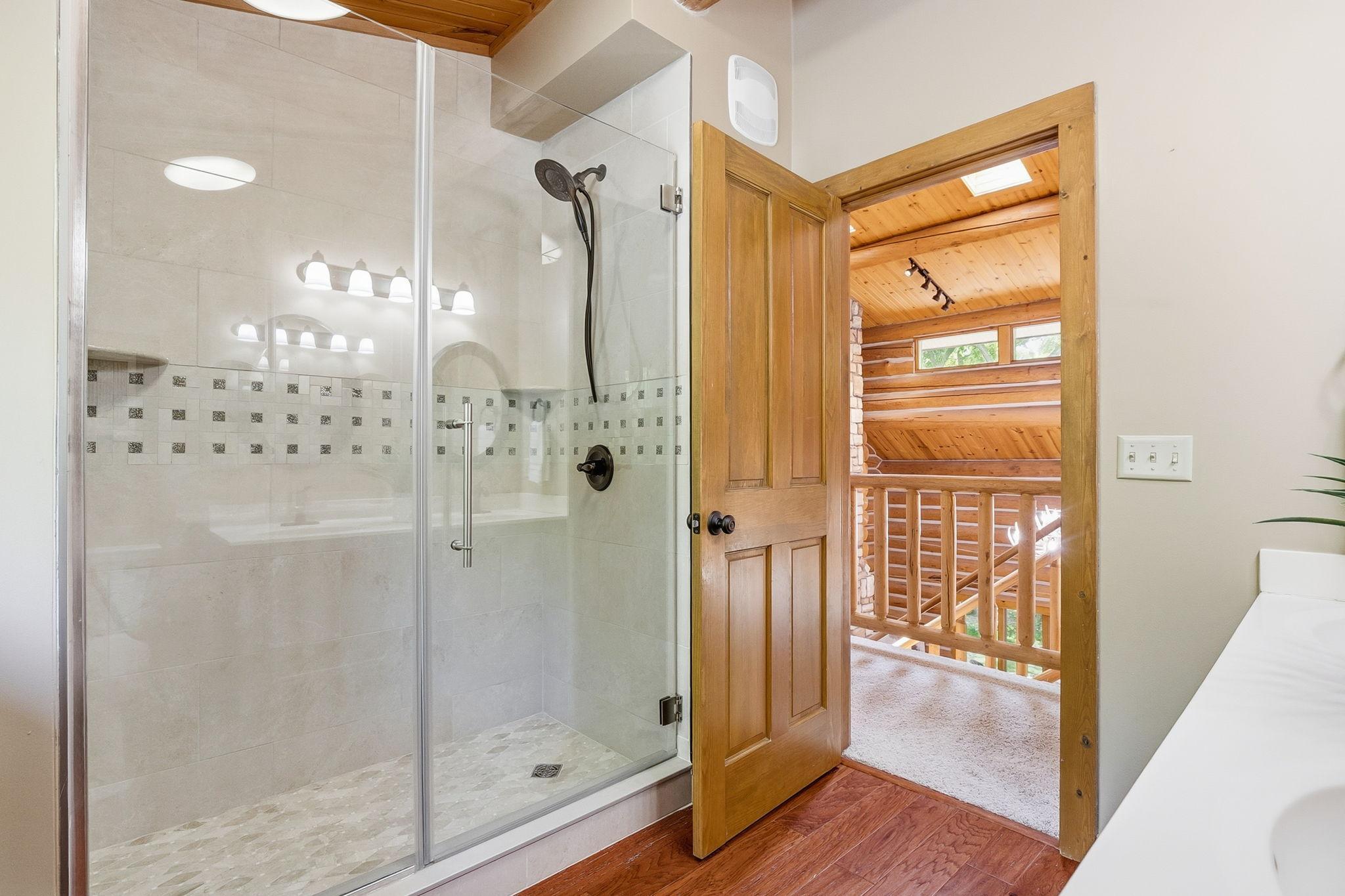 An upper-level 3/4 bath featuring a dual-sink vanity and walk-in shower, blending everyday convenience with warm log-home character.