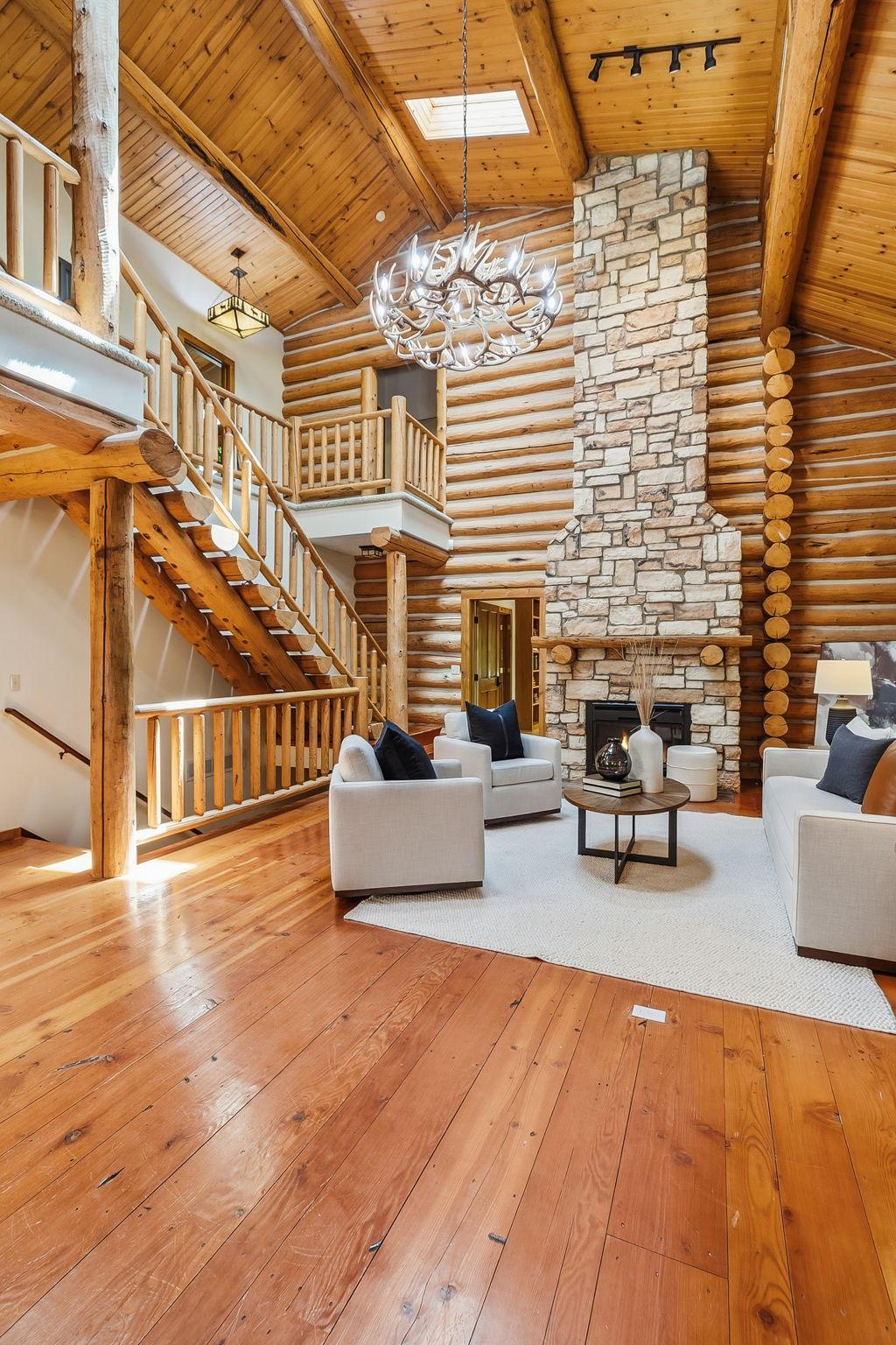 A breathtaking great room featuring a floor to ceiling stone fireplace, rich log craftsmanship, and expansive windows that fill the space with warmth and natural light.