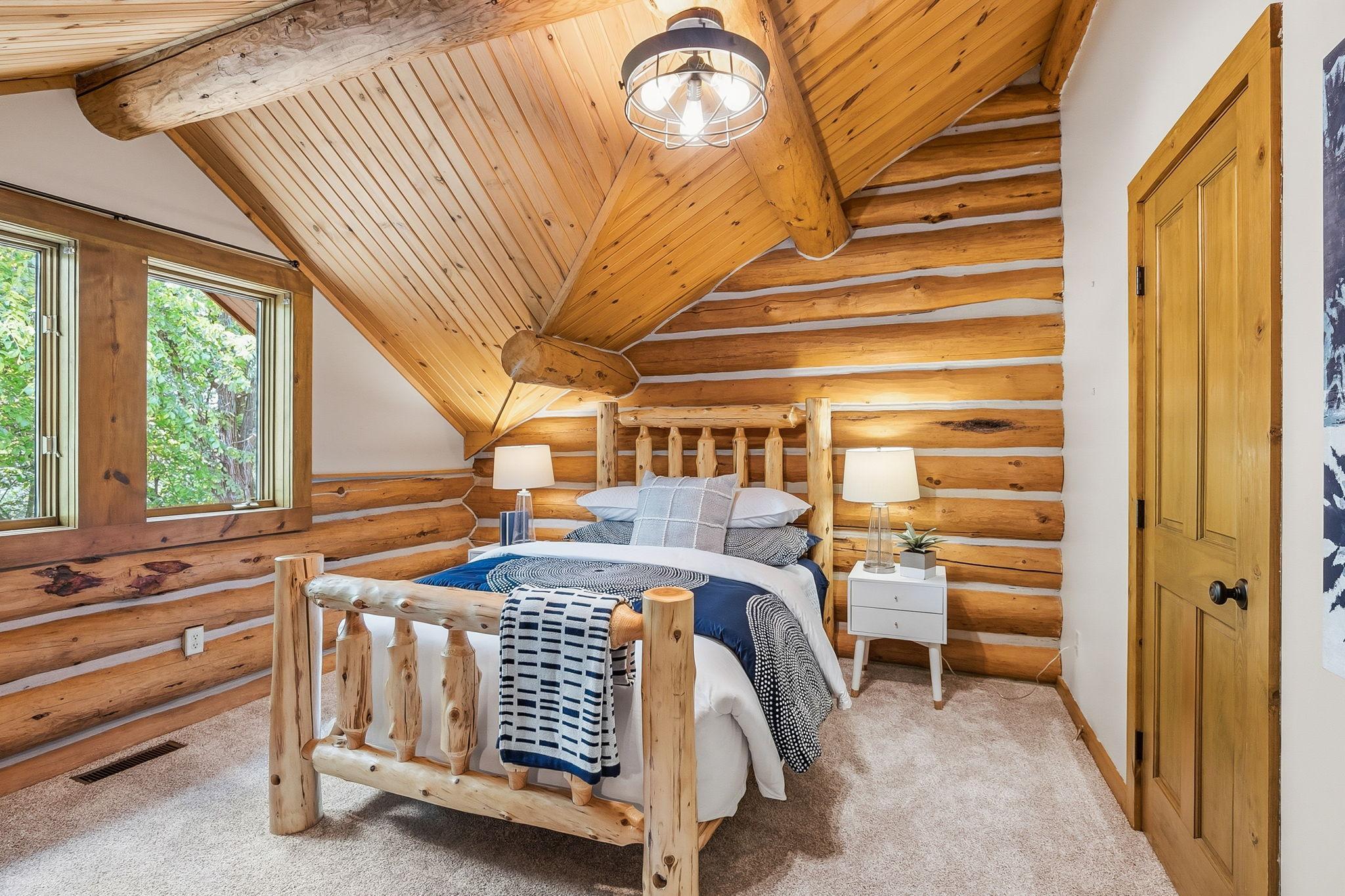 A charming upper-level bedroom with vaulted wood ceilings and rich log detailing, offering a cozy, cabin-inspired retreat filled with natural light.