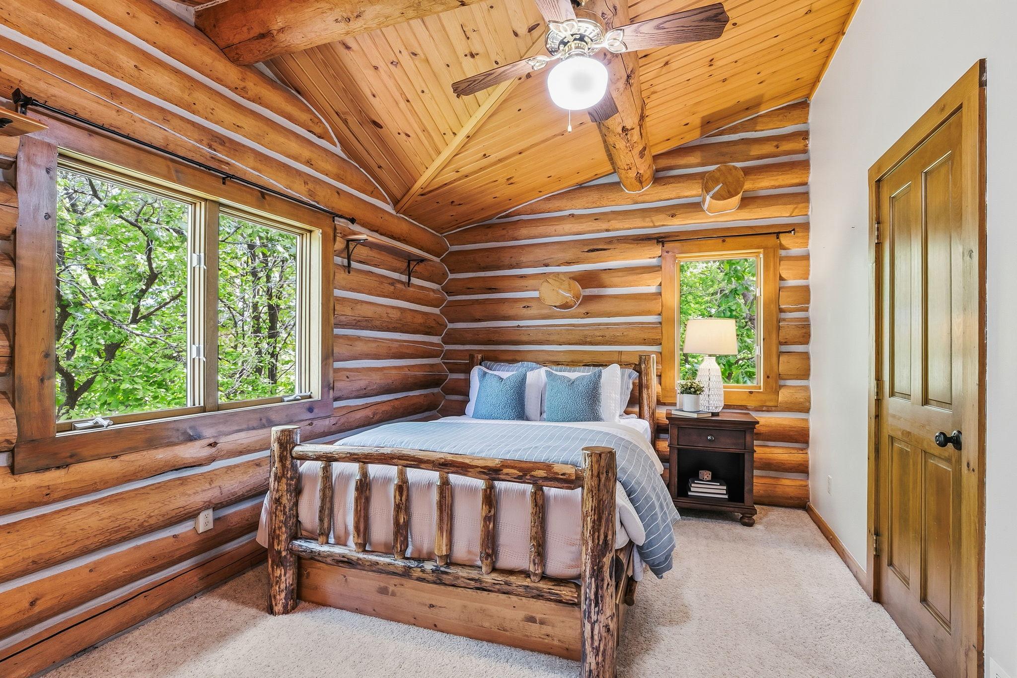 A cozy upper-level bedroom featuring vaulted wood ceilings and rustic log accents, offering a warm, cabin-style retreat with inviting character.