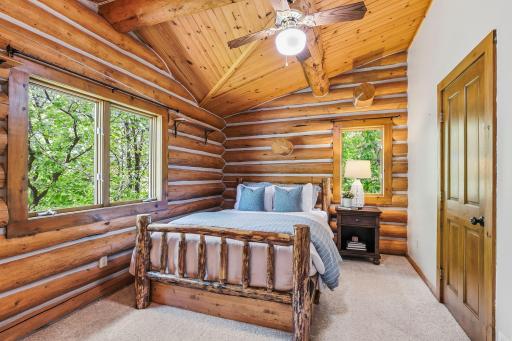 A cozy upper-level bedroom featuring vaulted wood ceilings and rustic log accents, offering a warm, cabin-style retreat with inviting character.