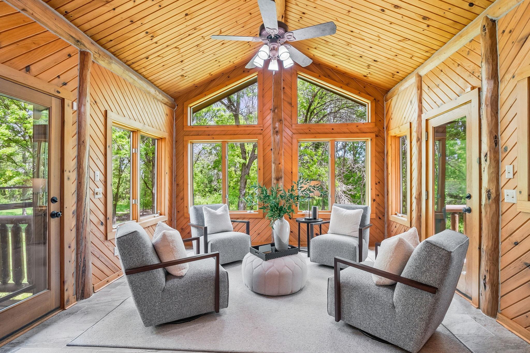 A sun-drenched four-season porch with vaulted wood ceilings and panoramic windows, offering a peaceful, nature-filled retreat perfect for year-round relaxation and seamless indoor-outdoor living.