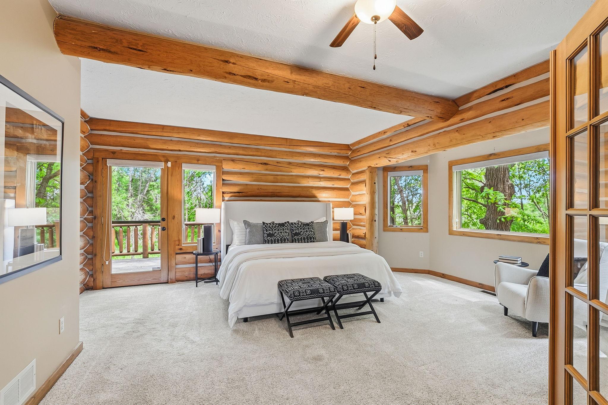 A spacious main-level primary suite wrapped in rich log character, featuring abundant natural light and private deck access, creating a peaceful retreat that seamlessly blends indoor comfort with the outdoors.