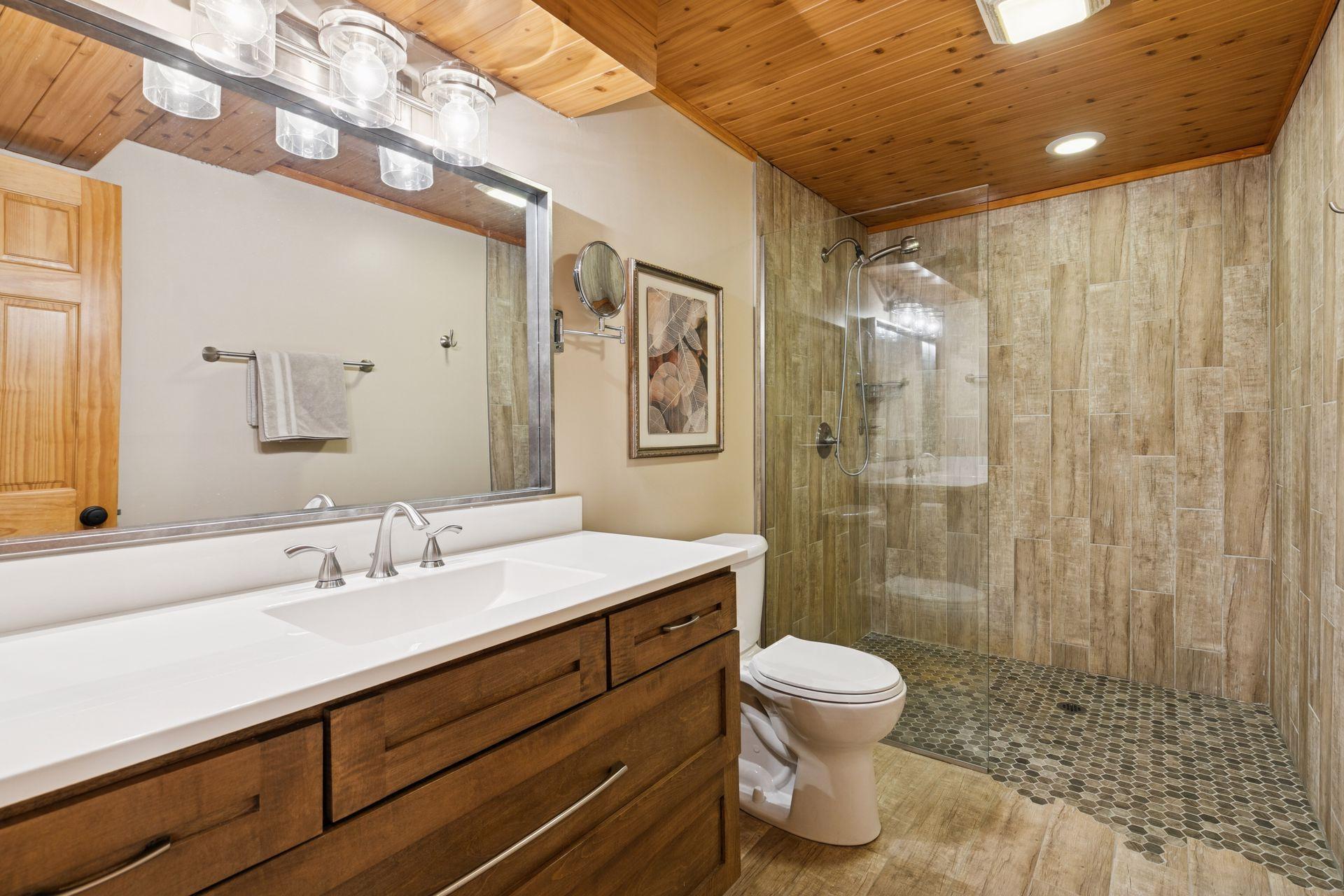 The lower-level bathroom features a stunning tiled shower complemented by a tongue-and-groove ceiling, combining elegance with a warm, textured design.