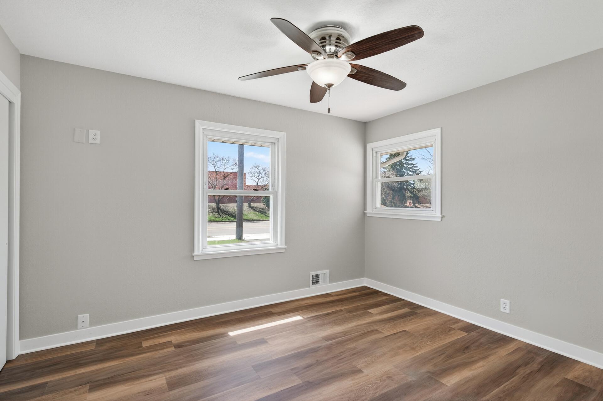 First main level bedroom featuring dual windows, hard surface floors, neutral tones, and a ceiling fan.