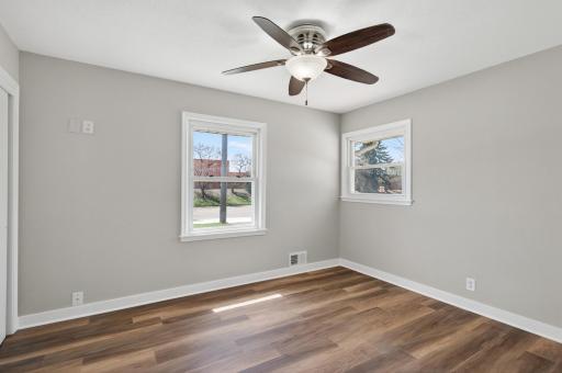 First main level bedroom featuring dual windows, hard surface floors, neutral tones, and a ceiling fan.